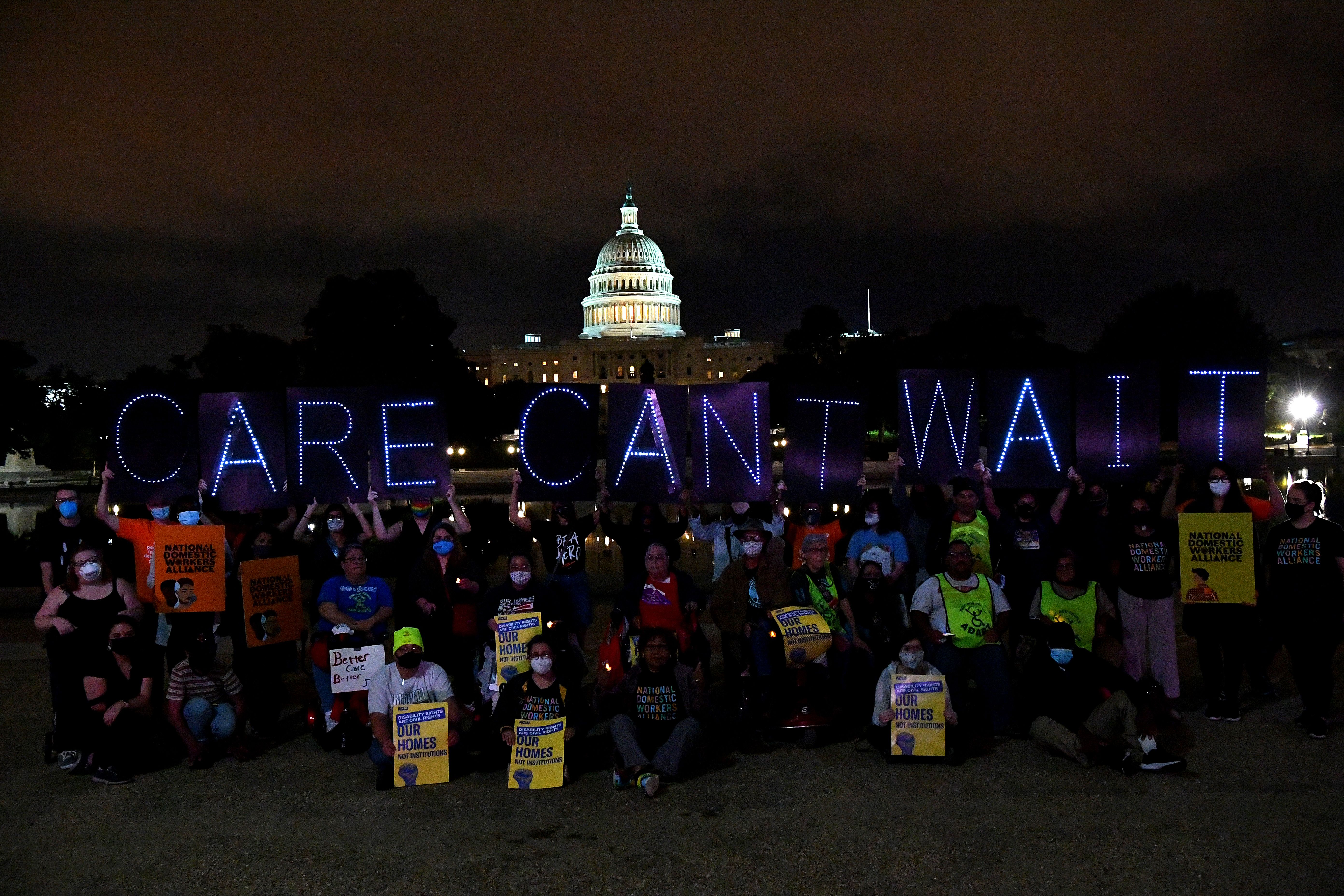 Crowds hold illuminated signs in front of the US Capitol at night. "Care Can't Wait".