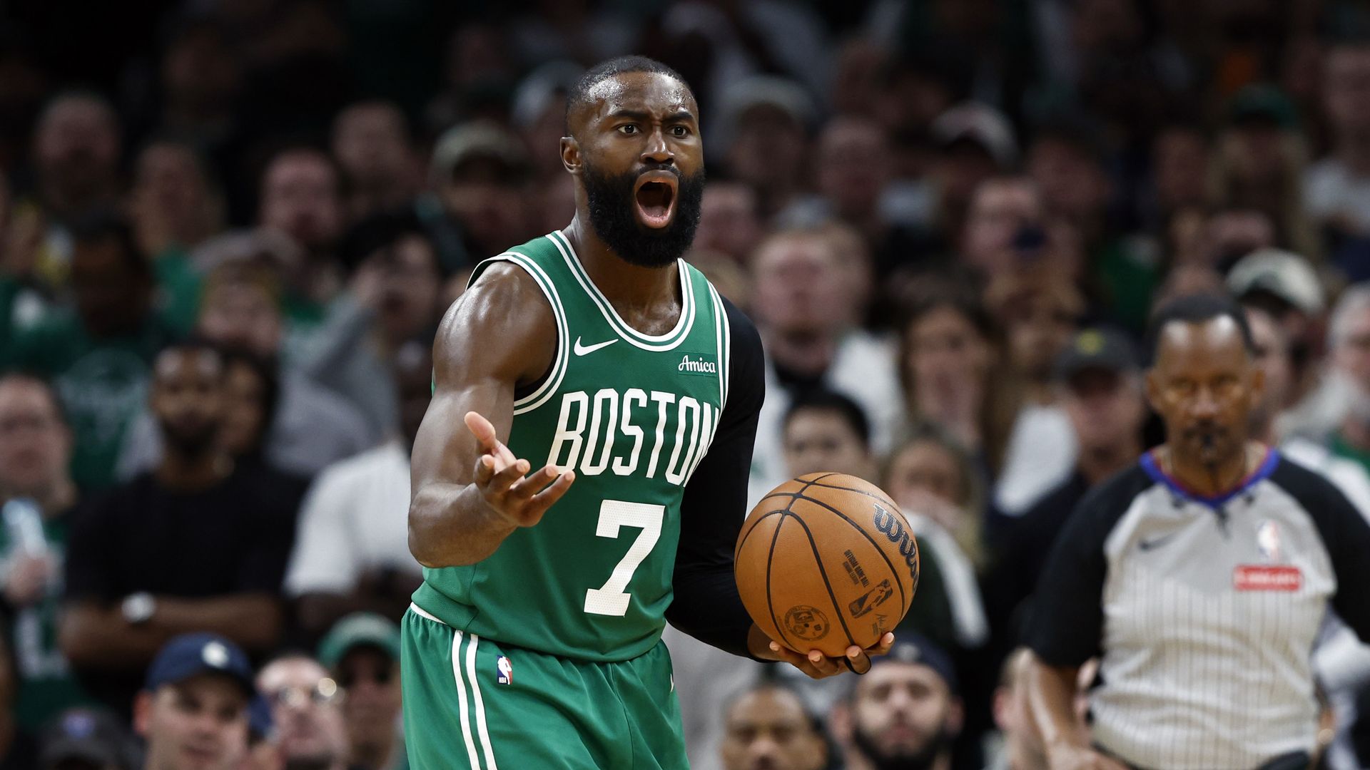 Jaylen Brown gestures angrily while holding a basketball during a game. He's wearing a green Celtics jersey with white lettering.