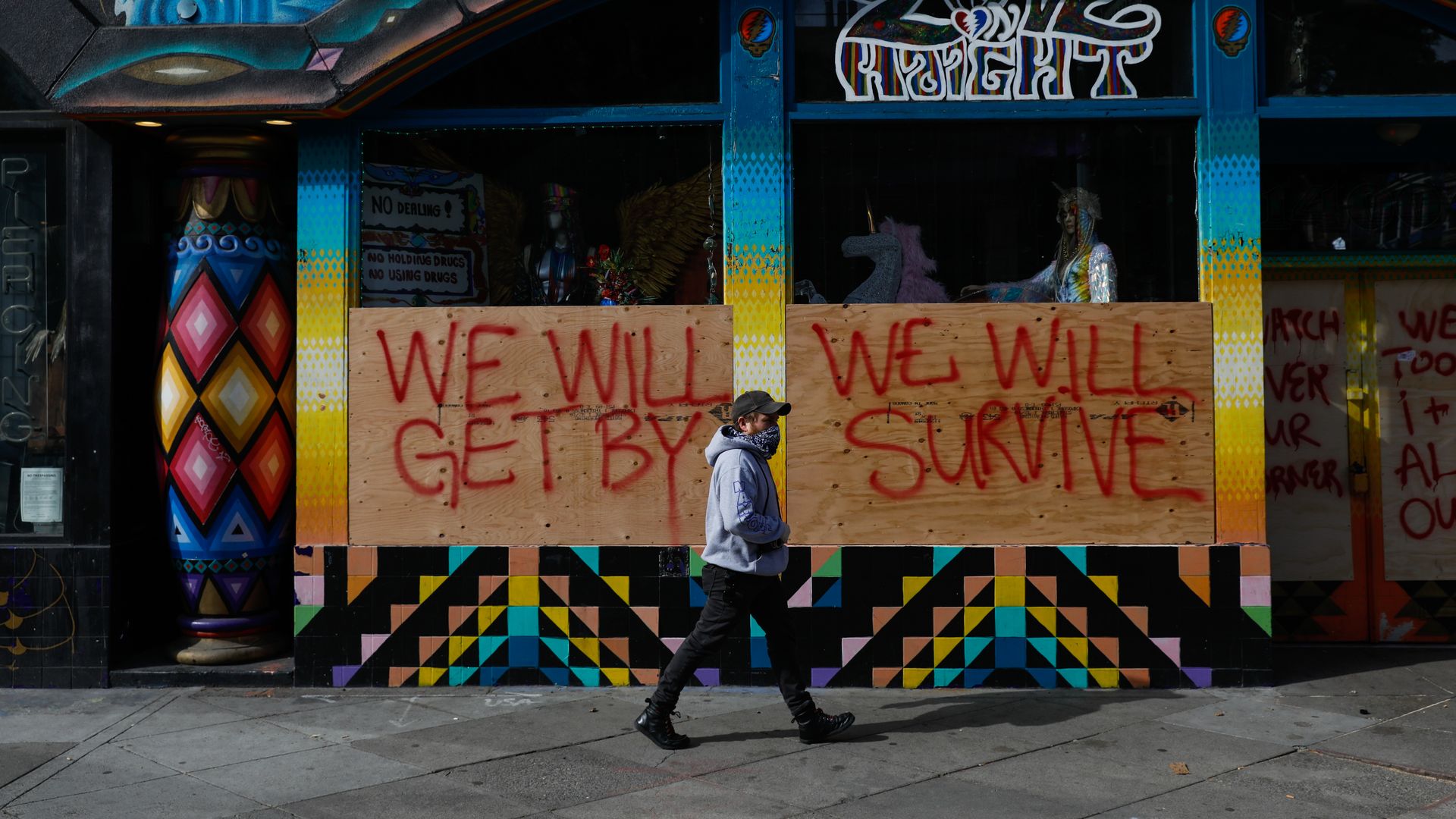Photo of boarded-up shops with the words "We will get by, we will survive" written on the boards