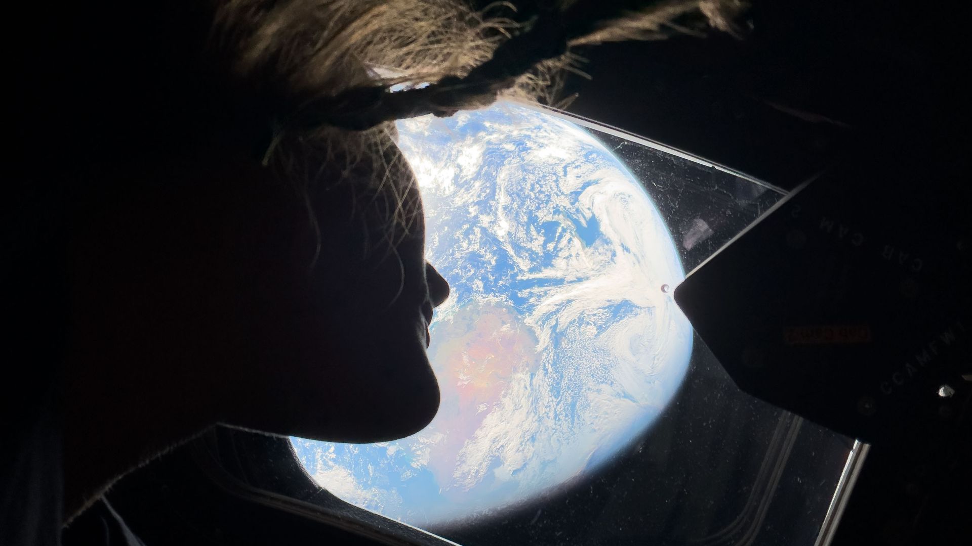 Astronaut Christina Koch looks out the window of the Orion spacecraft at Earth. 