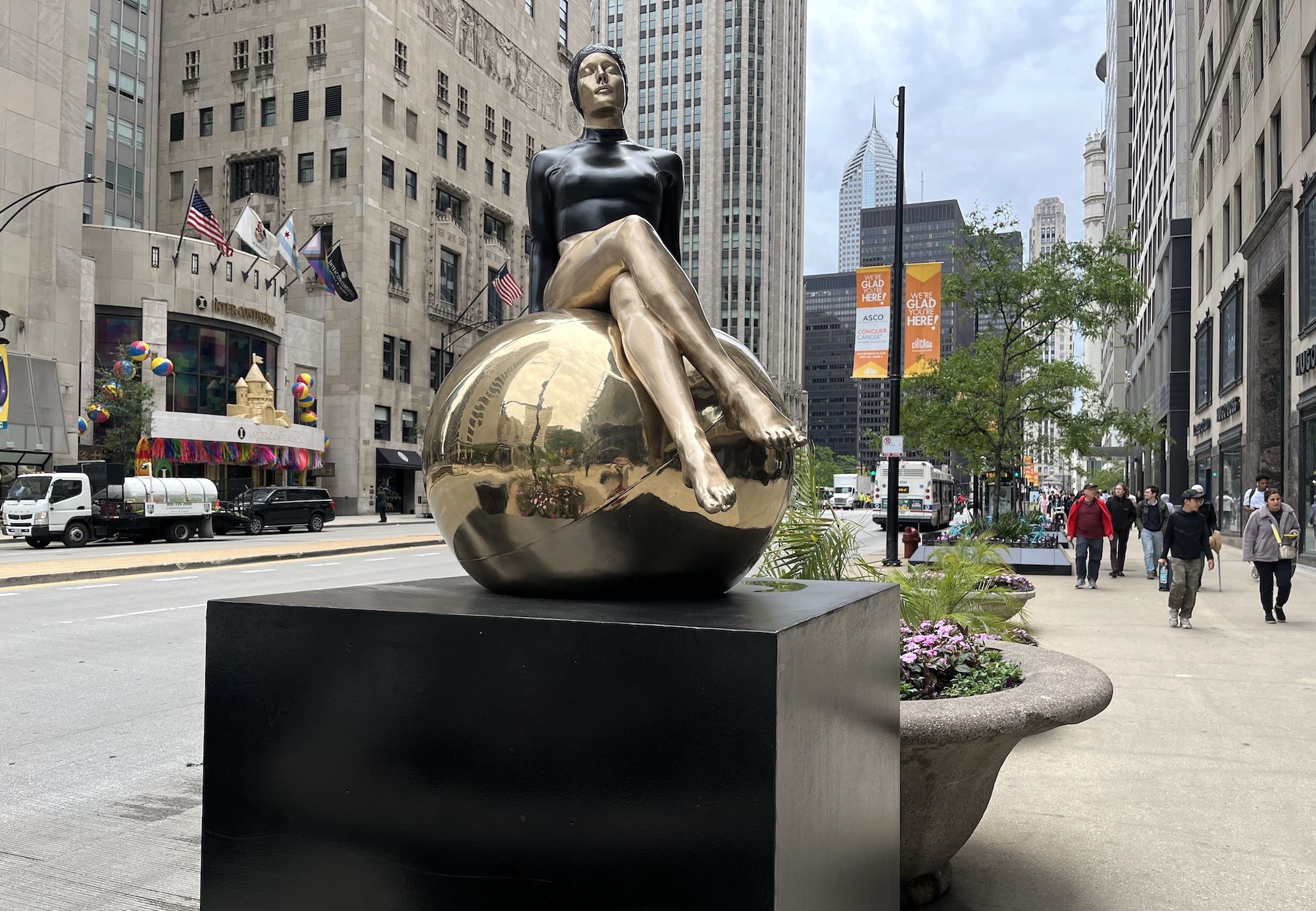 Sculpture of woman in black swimsuit sitting on a gold ball in front of Chicago's Michigan Avenue.