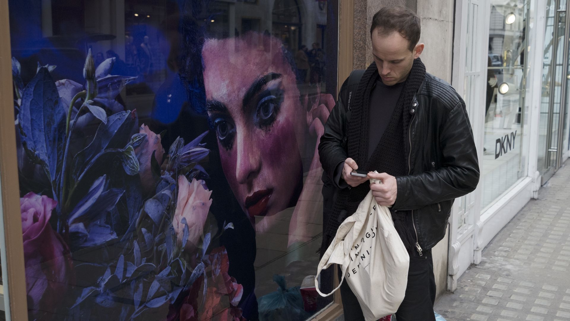 Photo of a man using his smartphone while walking by a mural