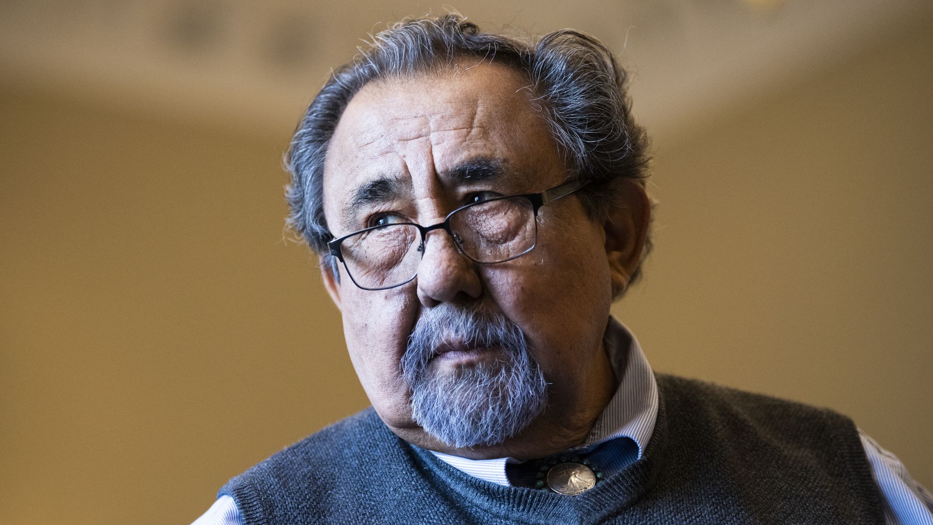 Rep. Raúl Grijalva, wearing a sweater and glasses, standing in a yellow room.