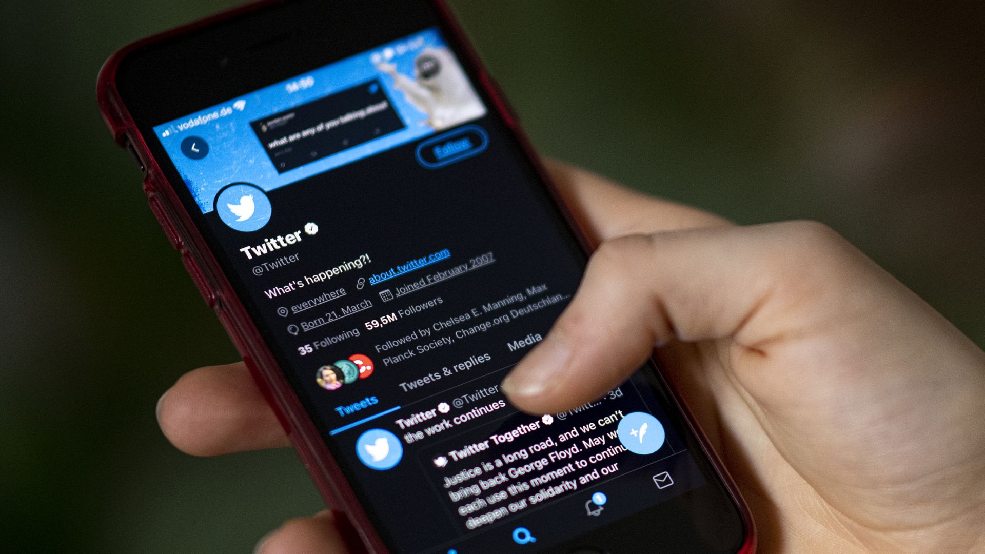 Photo of a hand holding a phone that shows the Twitter profile in the iOS Twitter app