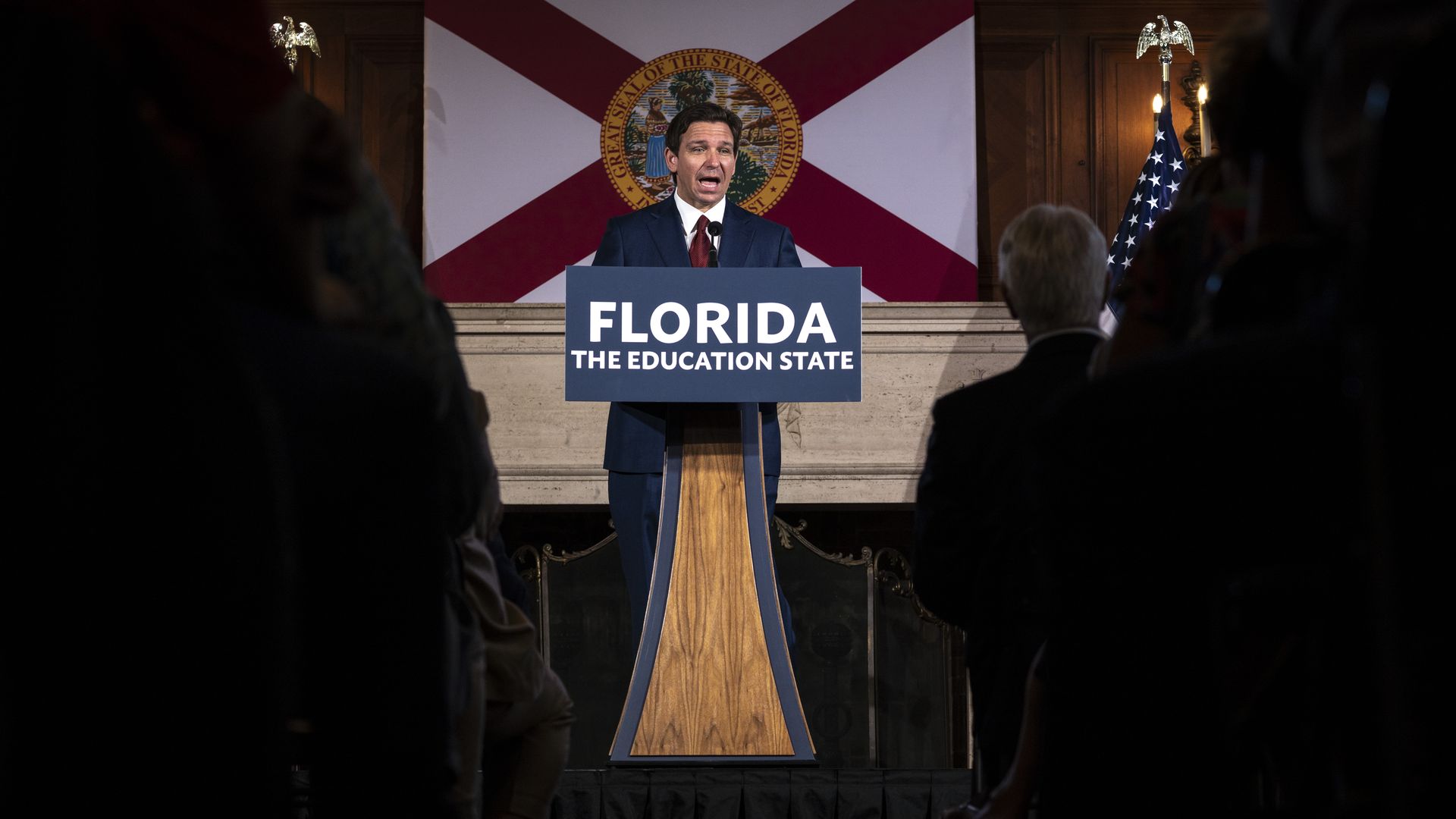 DeSantis stands at a lectern with a sign that reads "Florida The Education State." He is in front of the Florida flag.