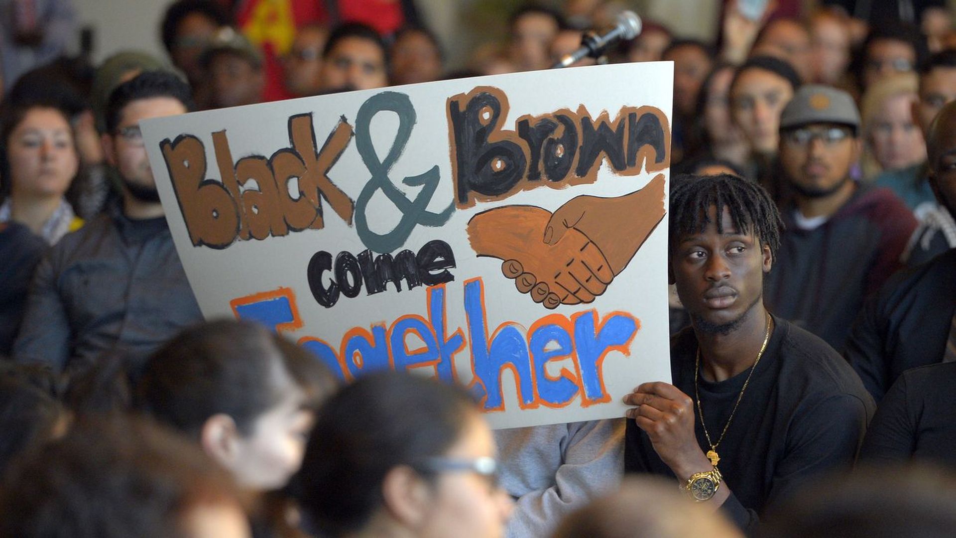 A man holds up a sign that says "black and brown come together" during a protest in Los Angeles