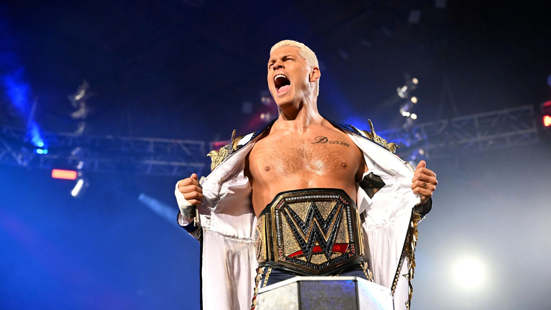 WWE star Cody Rhodes poses atop a ring corner showing off his championship belt while screaming. 
