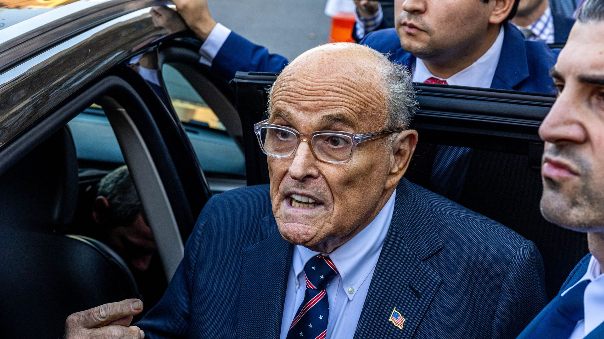 Rudy Giuliani is near a car door with people around him.