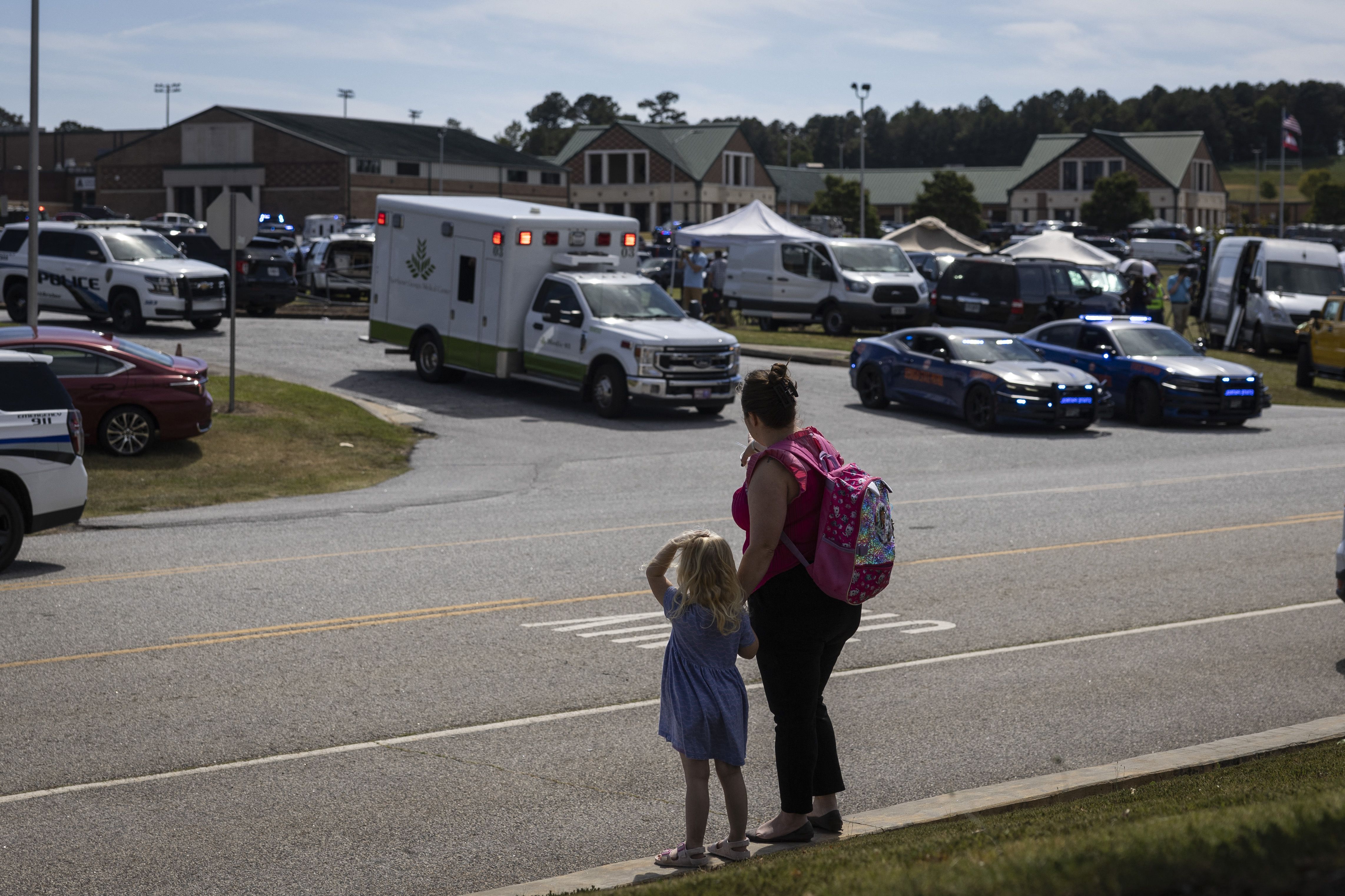 TOPSHOT - A young girl and her mother watch as law enforcement and first responders surround Apalachee High School in Winder, Georgia, on September 4, 2024, after a shooting was reported. Four people were killed and nine wounded in the school shooting on Wednesday, the Georgia Bureau of Investigatio