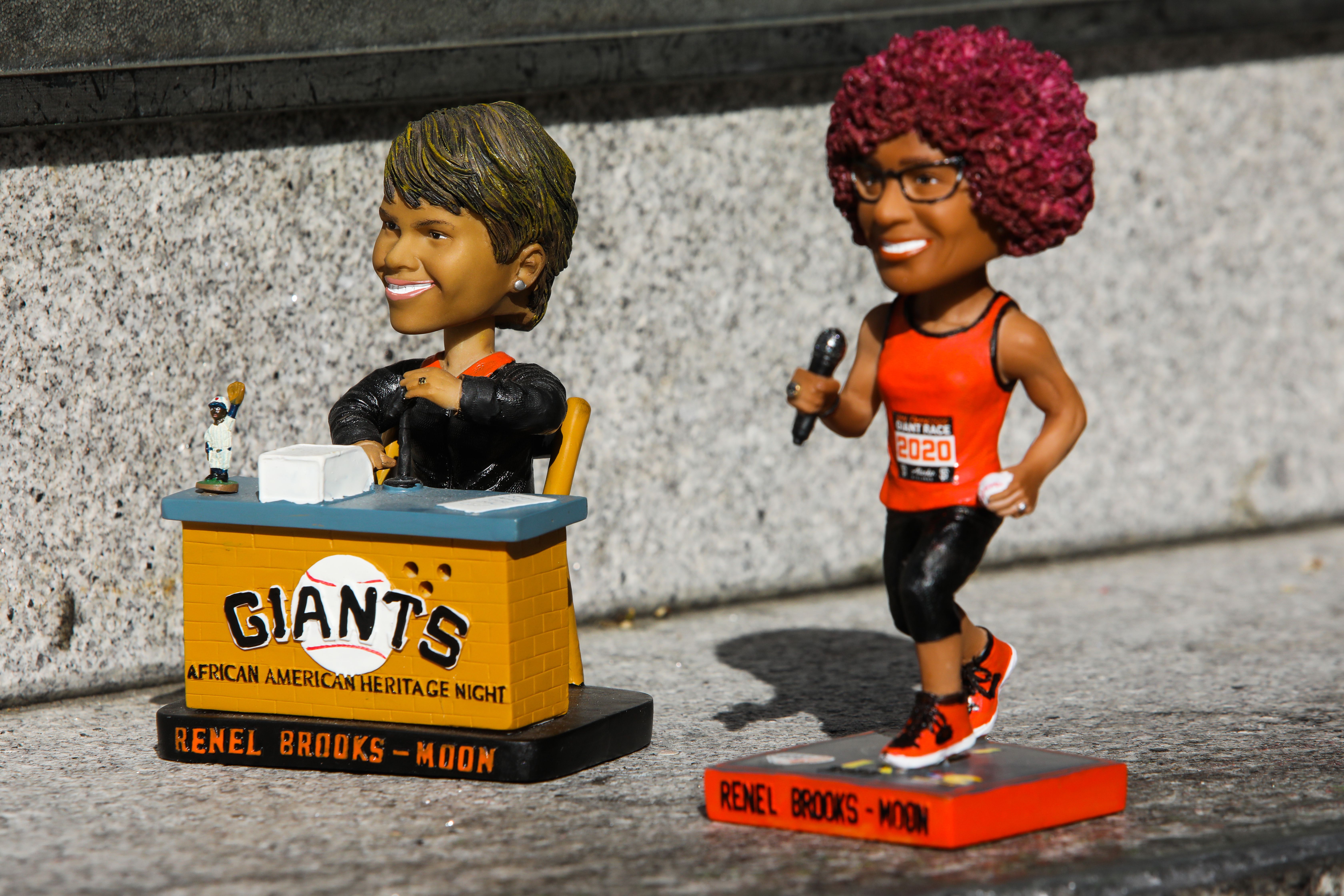 Photo of two bobbleheads of Renel Brooks-Moon, one sitting in her PA booth and another holding a microphone