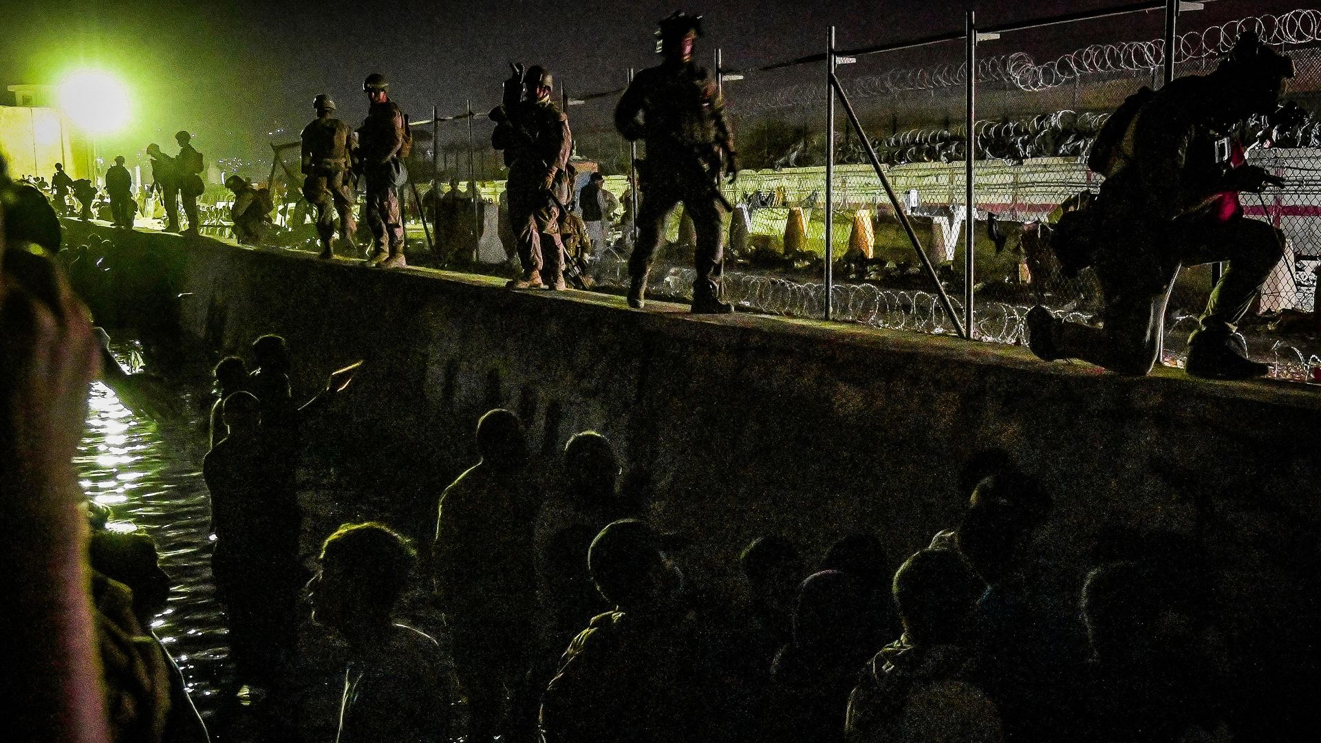 British and Canadian soldiers stand guard near a canal as Afghans wait outside the foreign military-controlled part of the airport in Kabul