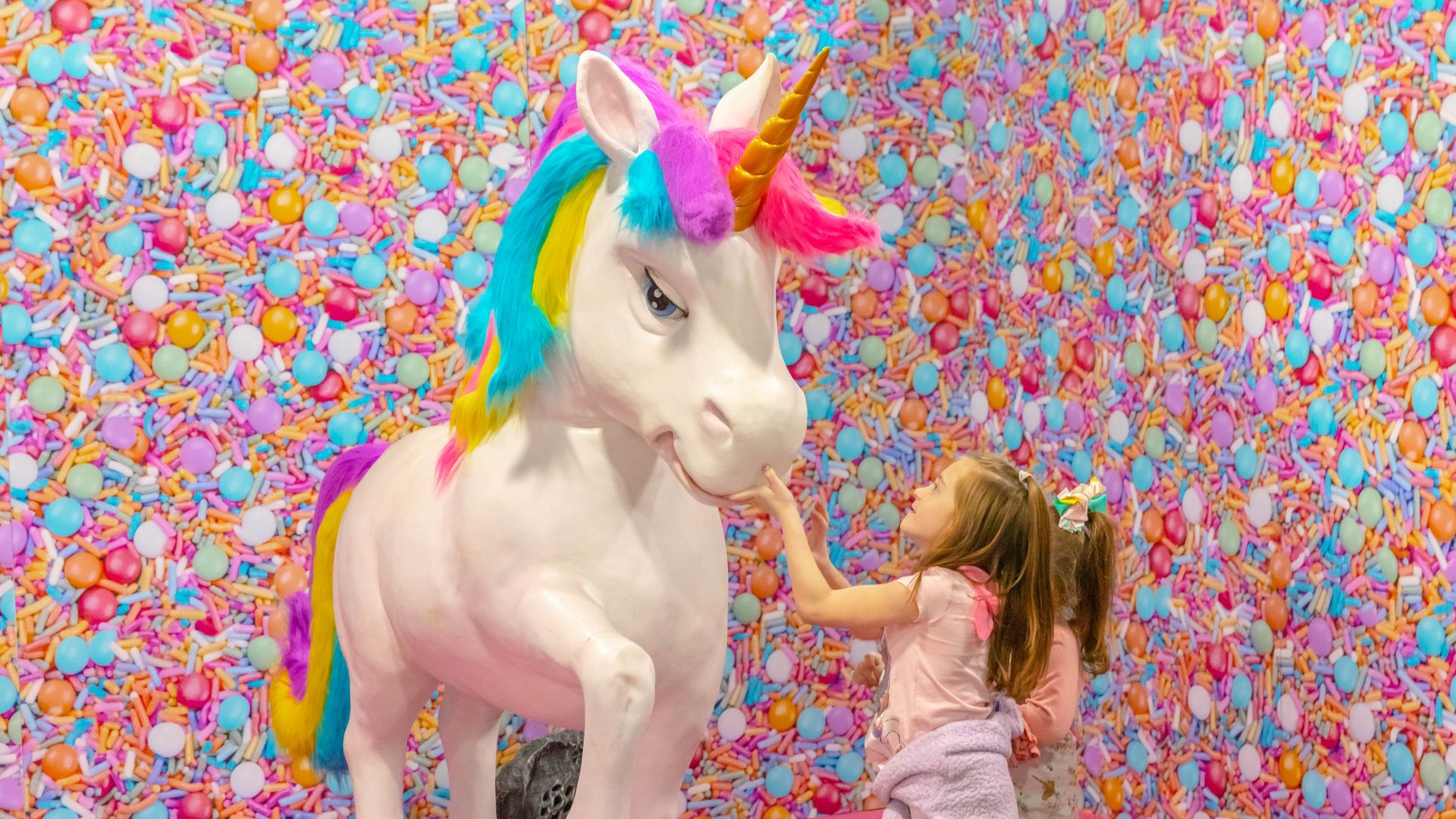 A small girl reaches up to pet a life-sized unicorn statue 