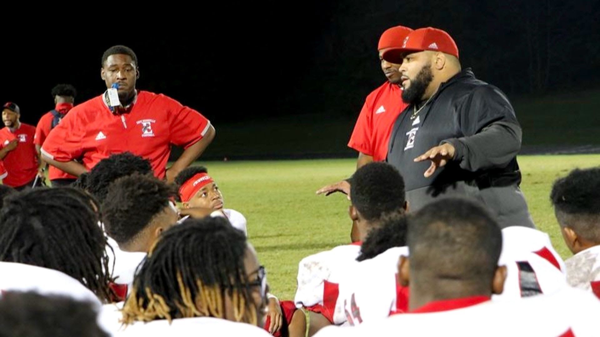 East Nashville High coach Jamaal Stewart in a black jacket addressing his kneeling team.