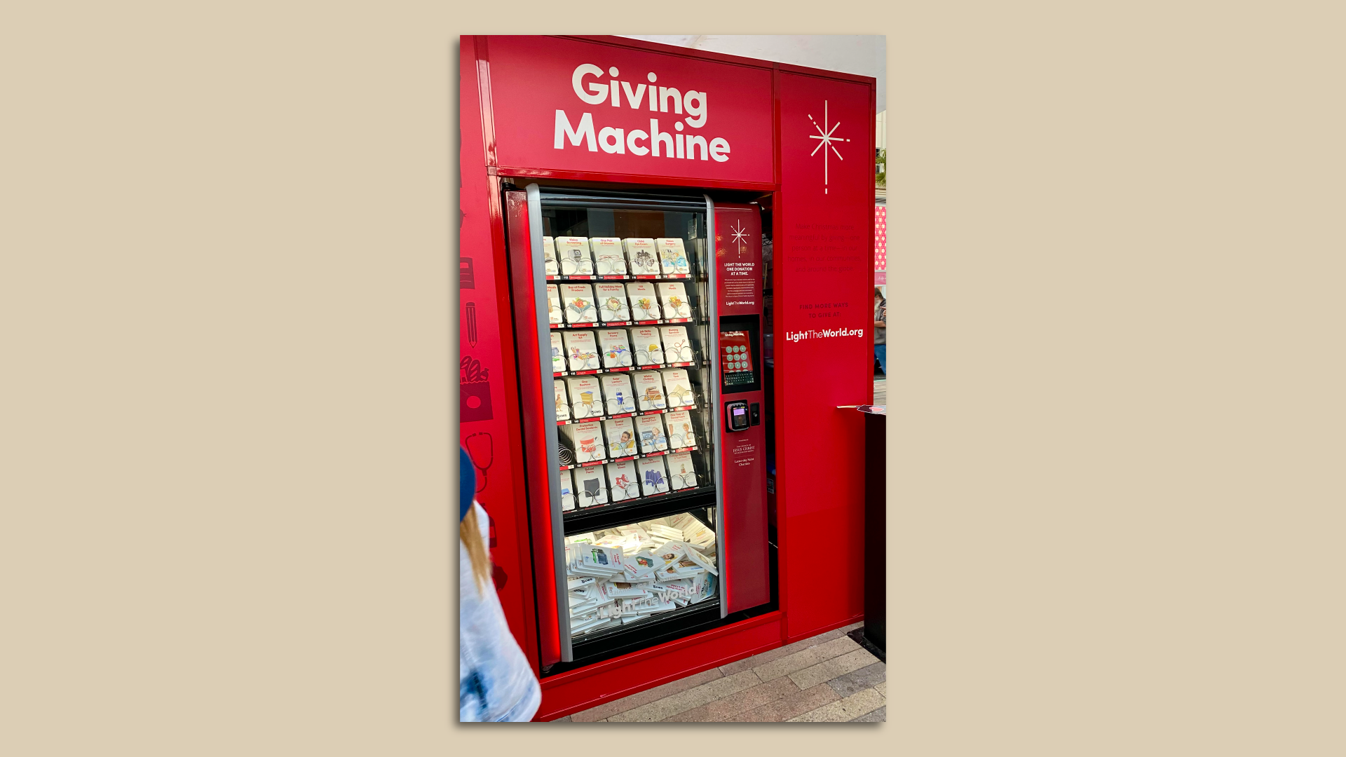 A red vending machine stocked with rows of cards with photos depicting items people can donate. 