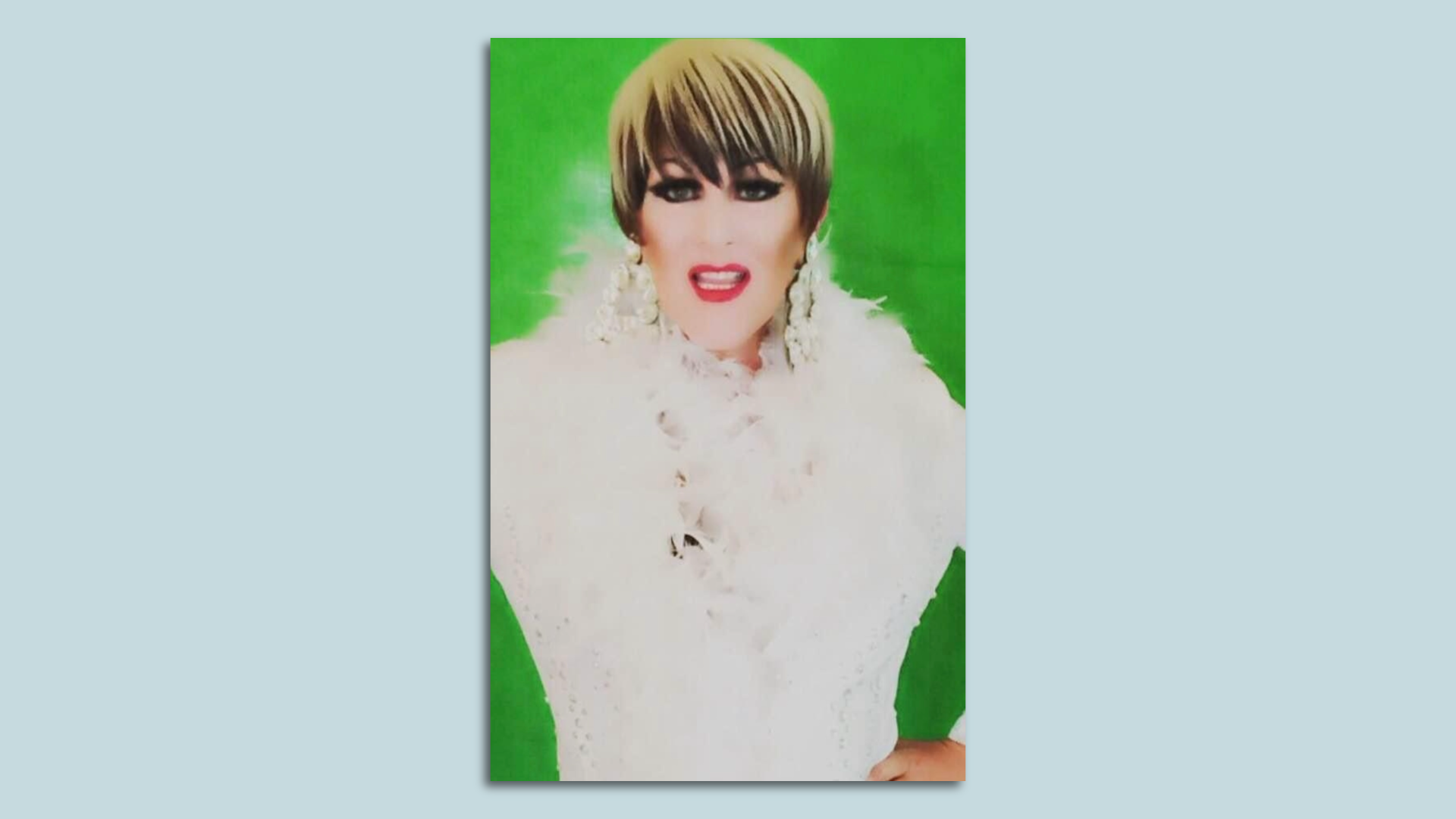 Sarasota drag performer Lindsay Calrton-Cline poses in a white feathered top in front of a bright green background.