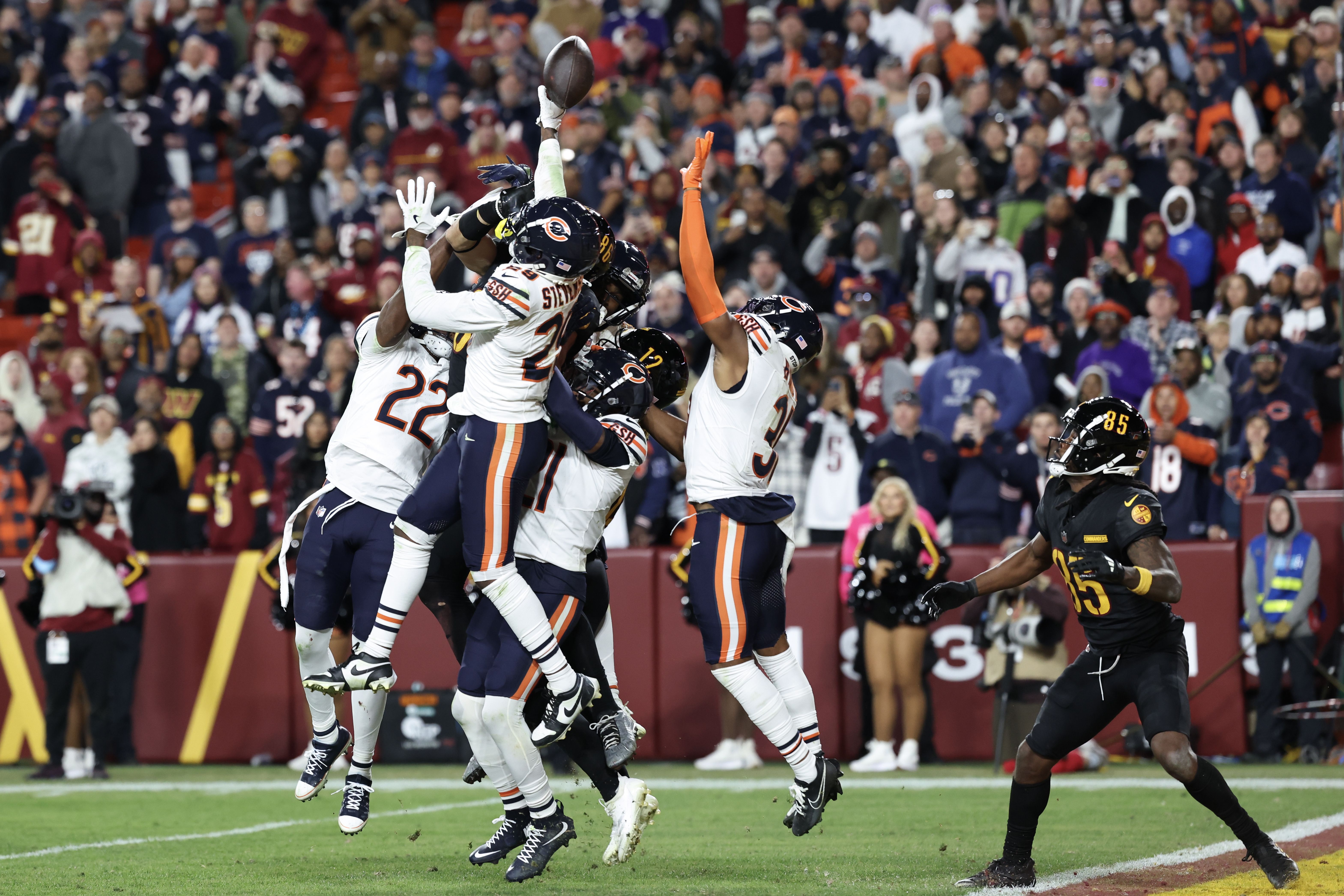 Photo of football players jumping to get a football on a field in a crowded stadium 