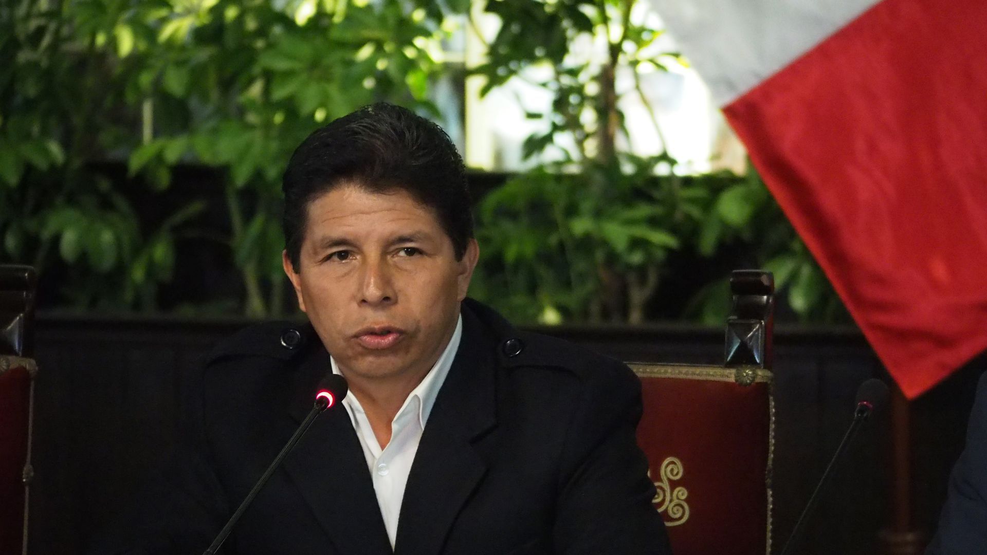 Peruvian President Pedro Castillo sits with a small microphone in front of him 