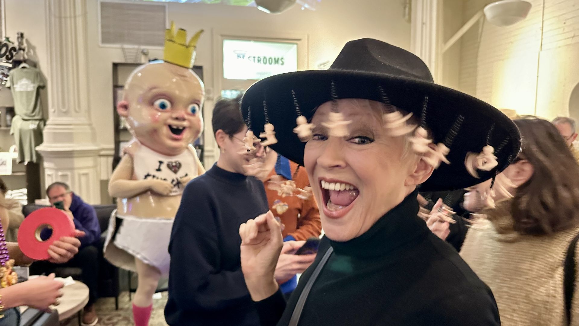 Photo shows a woman in a king cake hat with King Cake Baby in the background.