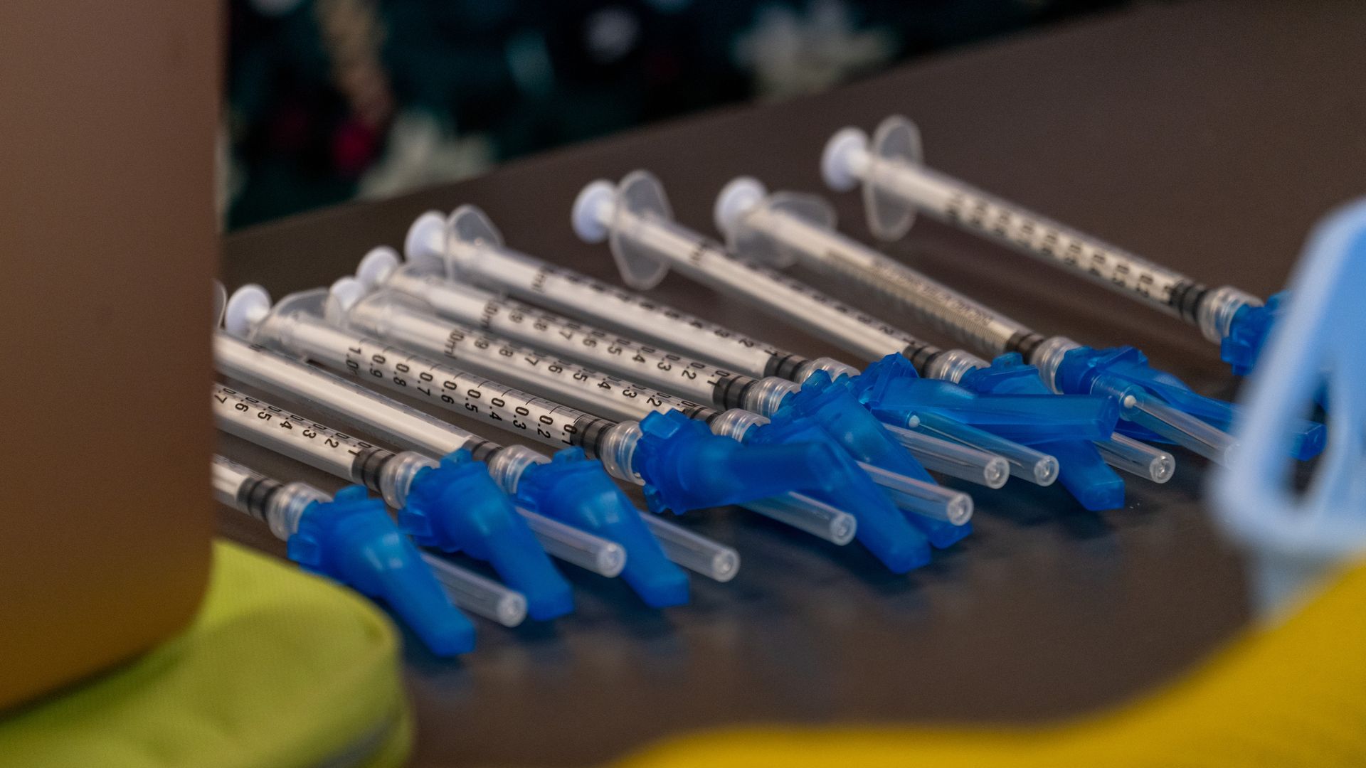 Several syringes with blue tips sit side by side on a wooden table