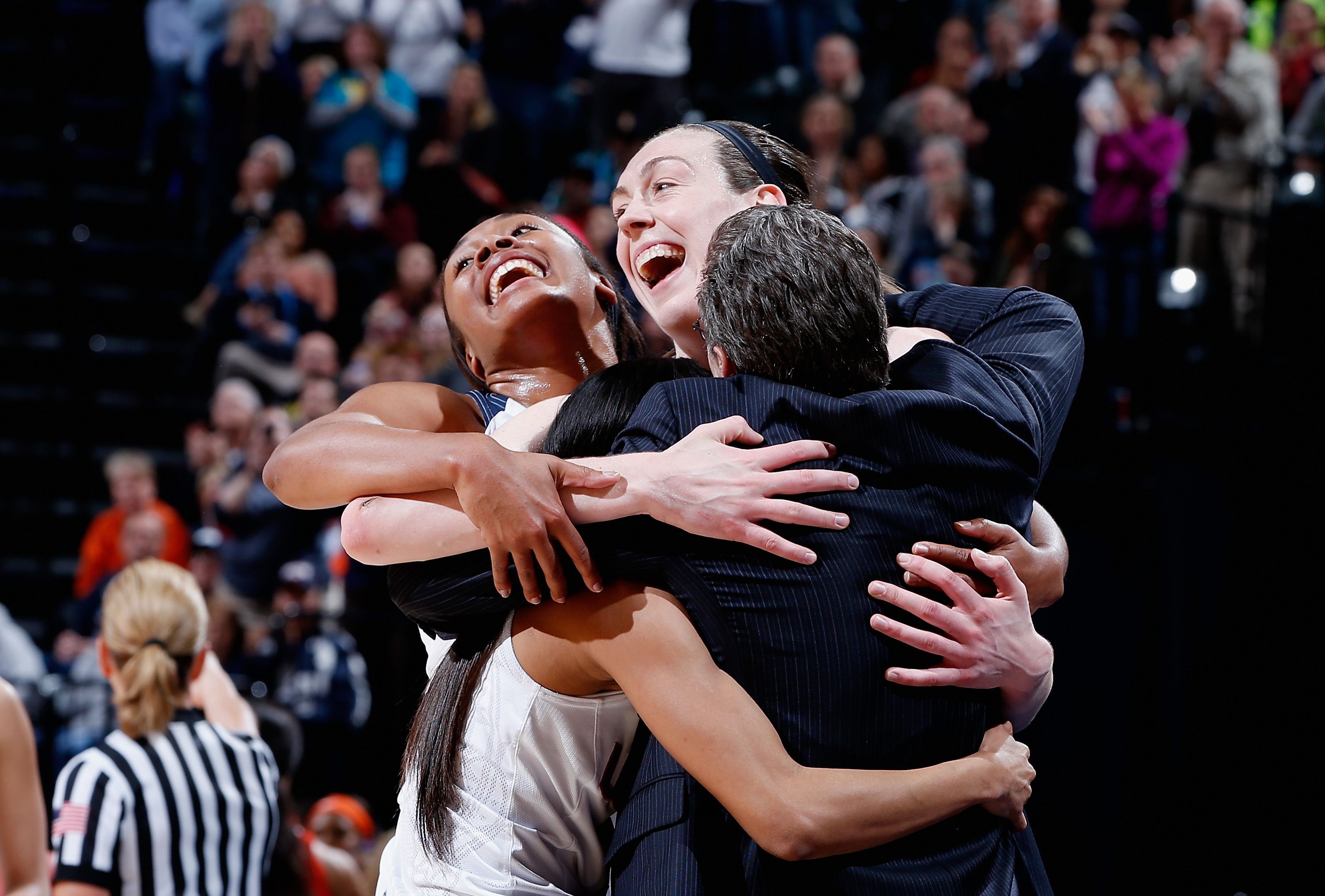 UConn women's basketball players and head coach celebrate in a hug. 