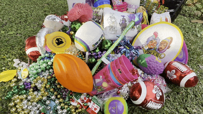 Image shows beads, footballs and other Mardi Gras parade throws on the grass.