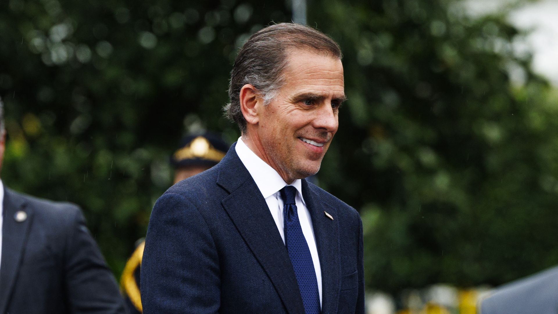 Hunter Biden wearing a blue suit and standing in front of trees surrounded by people.