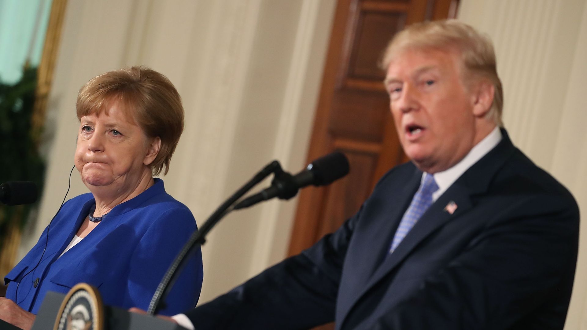 Angela Merkel puffs out her cheeks looking sideways at Trump.