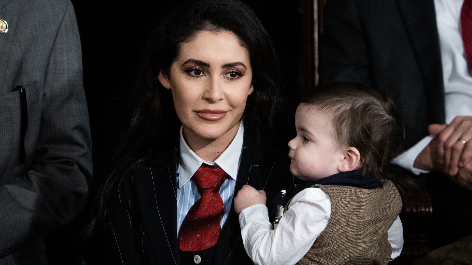Rep. Anna Paulina Luna, wearing a black suit and holding a child while surrounded by colleagues.