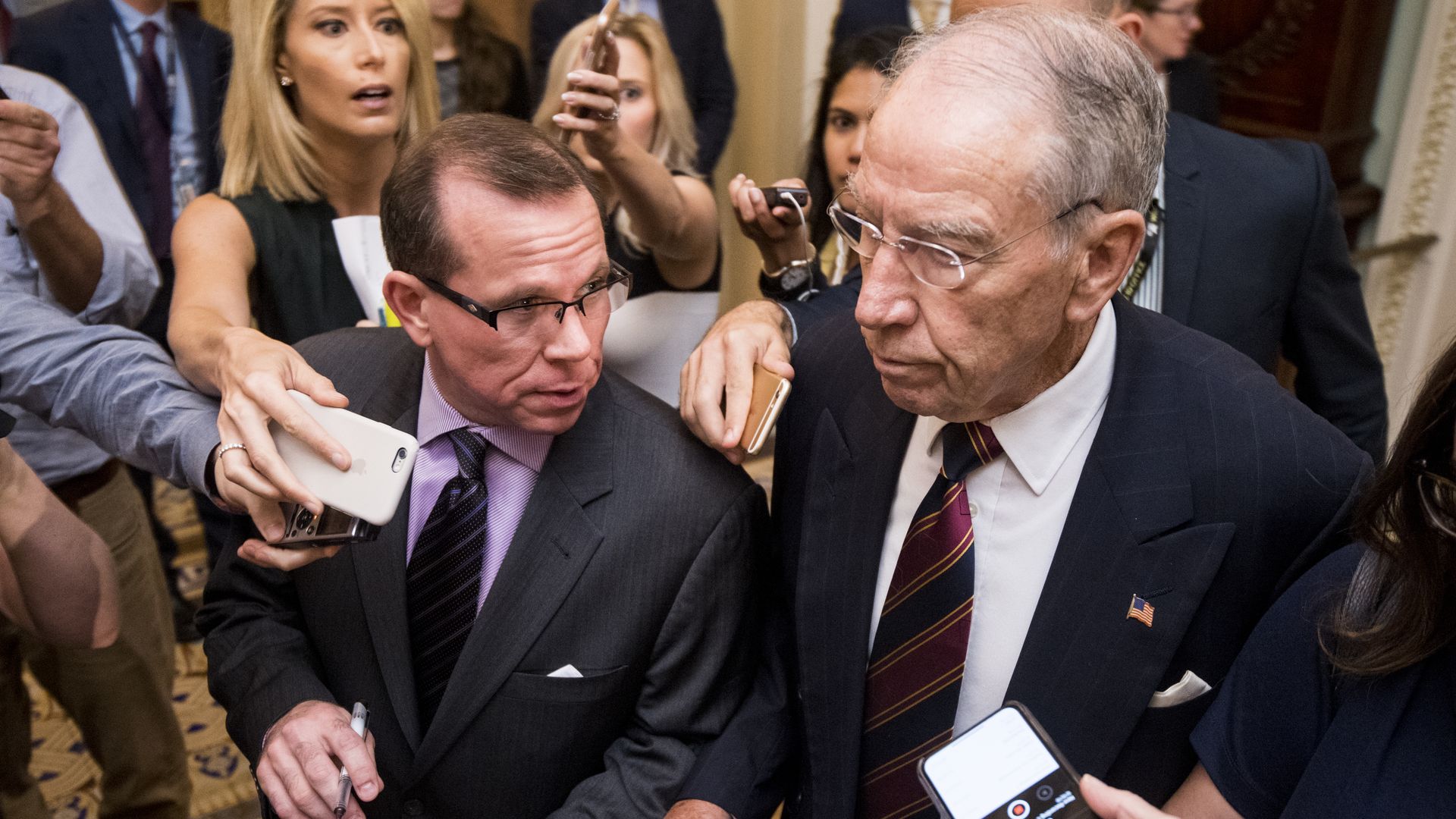 Senator Chuck Grassley surrounded by reporters asking questions. 
