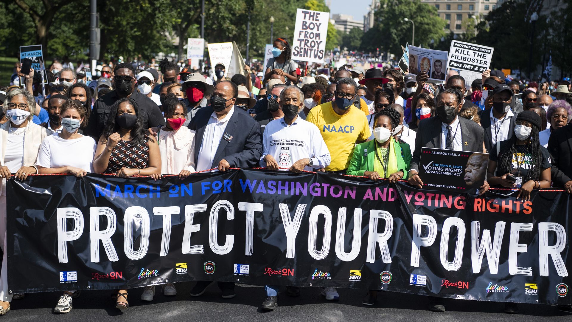 Photo of protesters holding a banner that says "Protect your power" as a crowd marches for voting rights