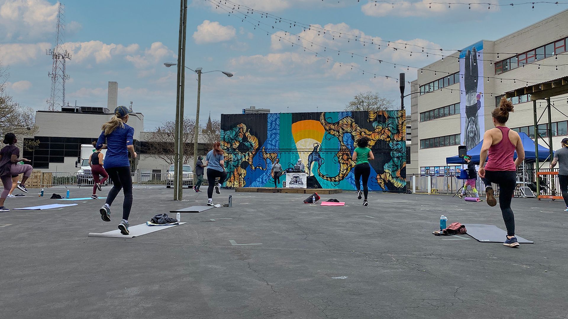 people exercising at a socially distanced exercise event in a city parking lot, with a colorful backdrop.
