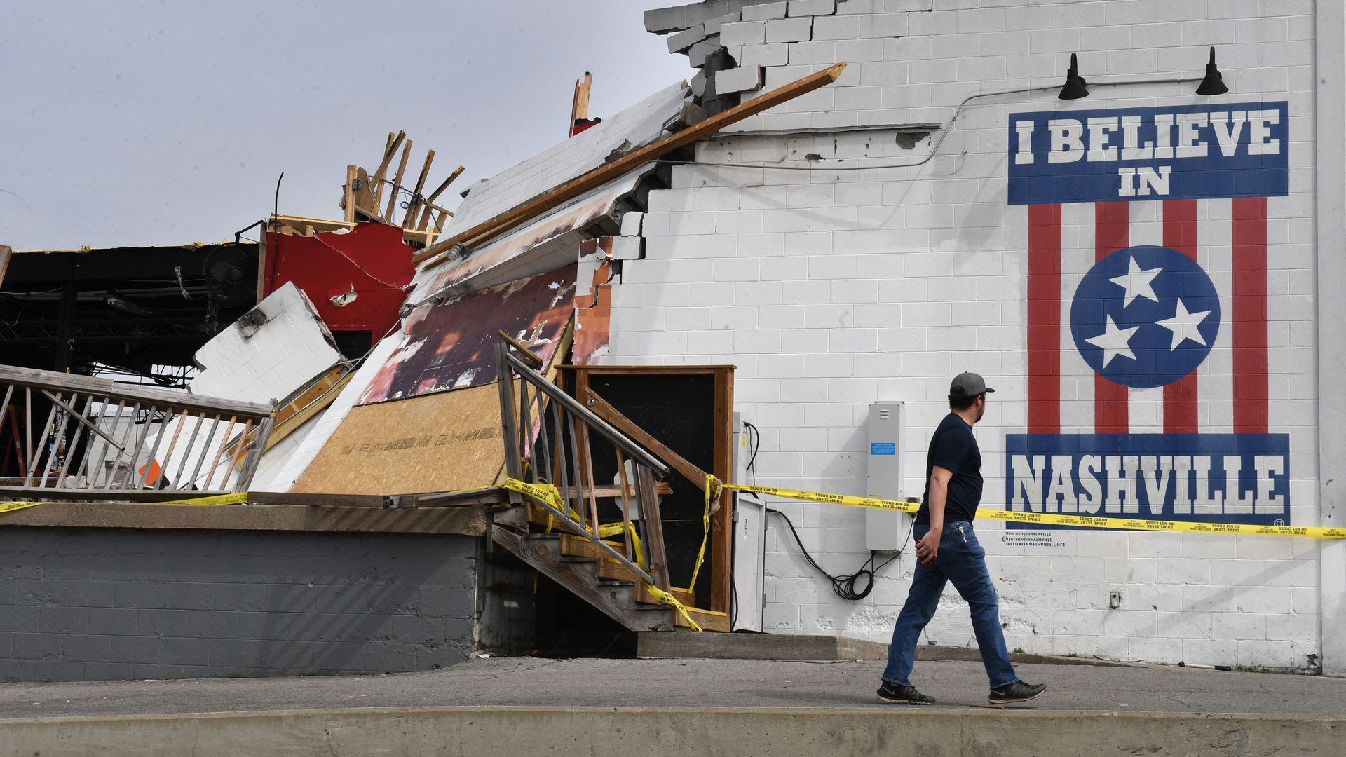 A person walks by a building damaged by the 2020 tornado. 