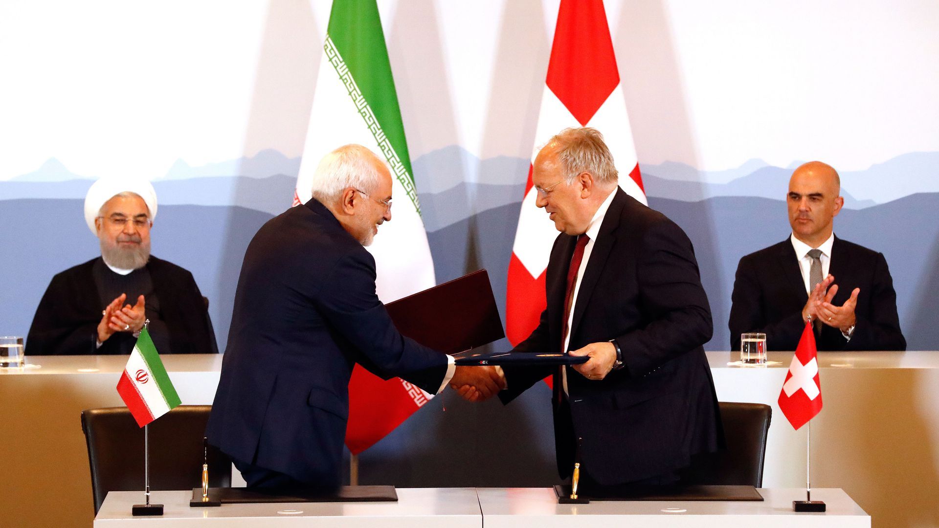 Photo of Iranian President Hassan Rouhani and Swiss President Alain Berset clap as Iranian and Swiss officials shake hands after signing an agreement in July