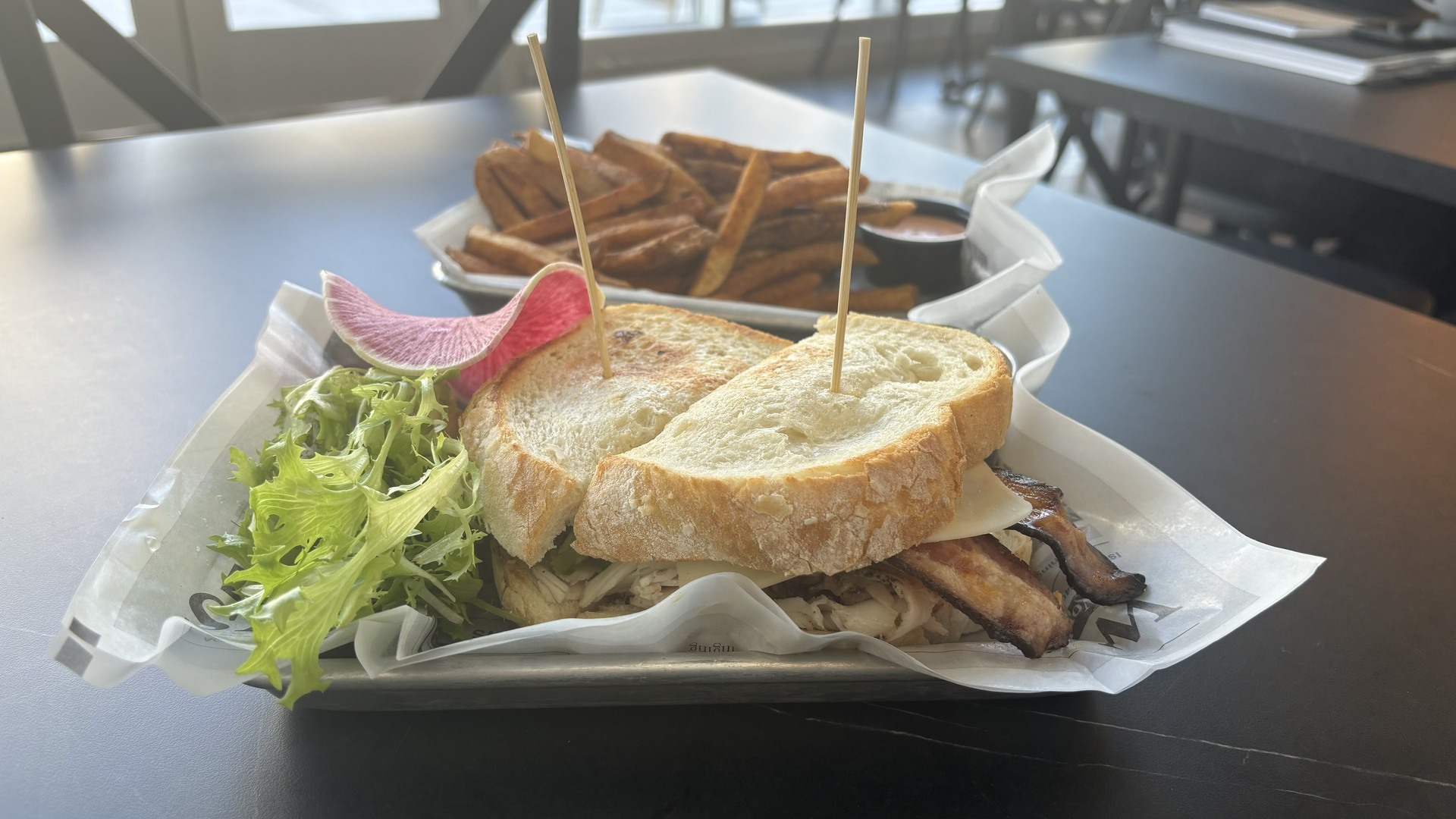 A sandwich sits next to a bed of lettuce and fries. 