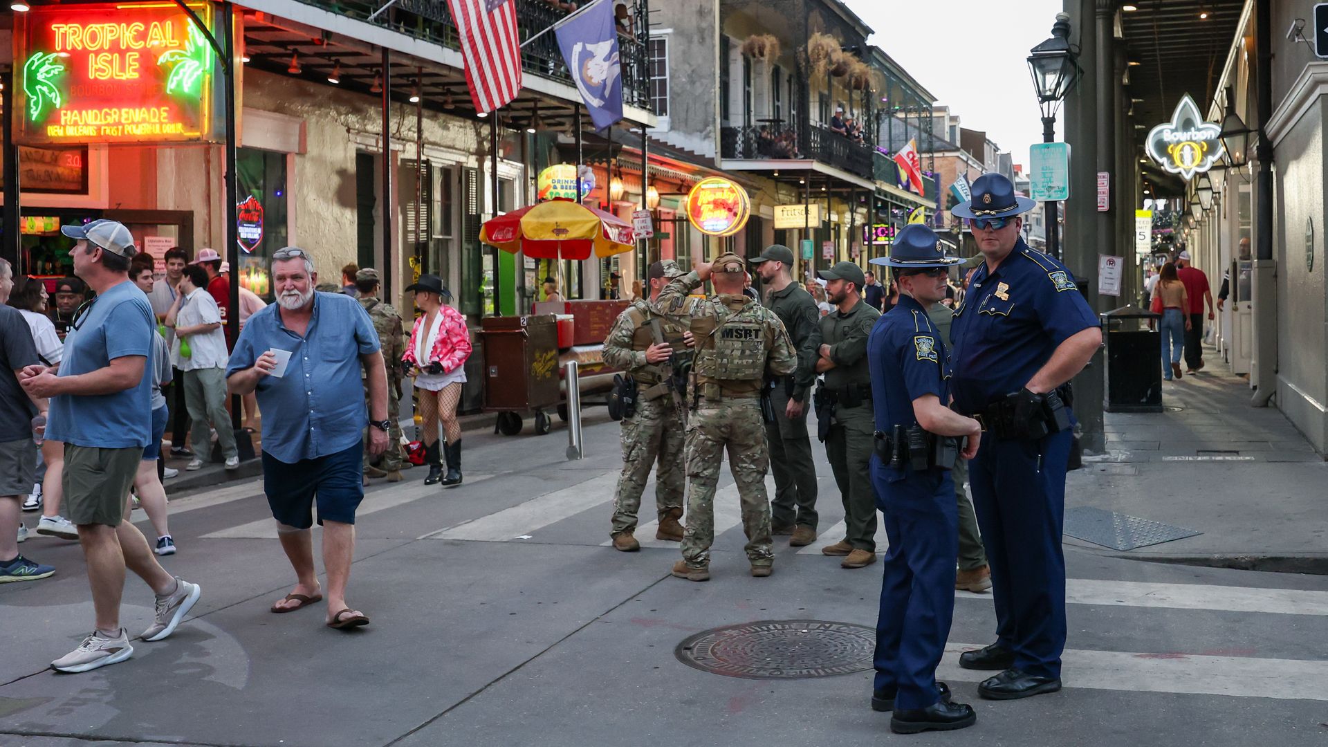 Crowds mill about on Bourbon Street as Louisiana State Police troopers and members of the National Guard huddle in separate groups near a street corner.