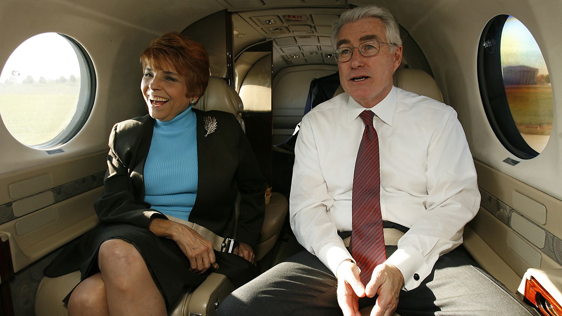 Judy Baar Topinka in a blue shirt and dark skirt suit sits next to Jim Edgar in a white dress shirt, red tie and dark suit paints on an airplane.
