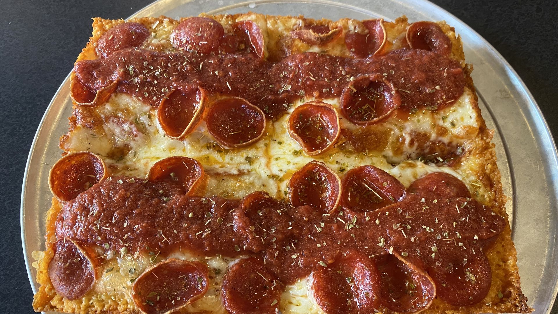 A square shaped deep dish pizza cut into four pieces with pepperoni and two rows of sauce on top. 