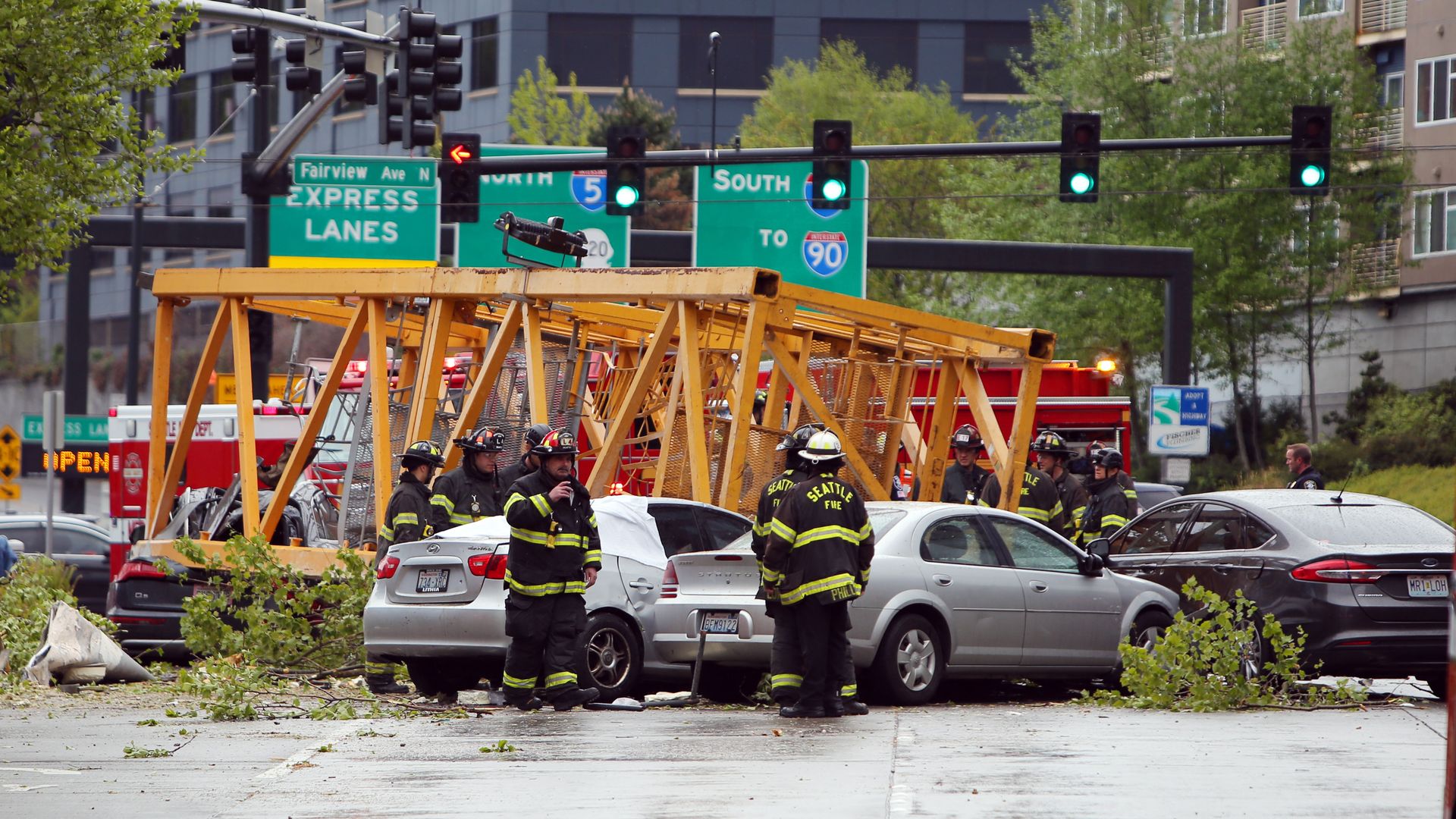 A rescue crew stands next to cars that are crushed under a yellow piece of a construction crane.