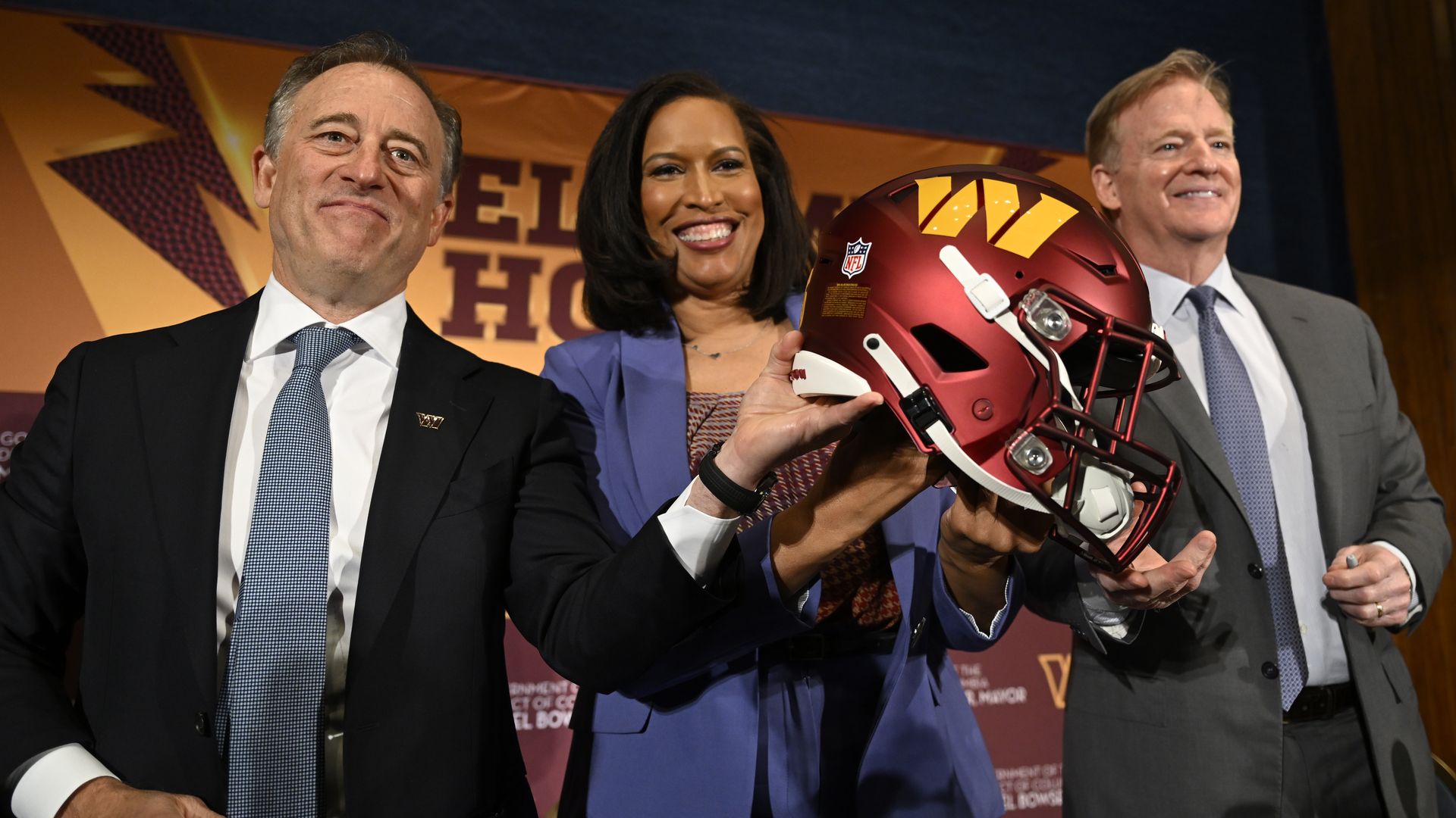 At a celebration for the Washington Commanders football stadium development announcement, team owner Josh Harris, D.C. Mayor Muriel Bowser, and NFL commissioner Roger Goodell hold a Commanders helmet.