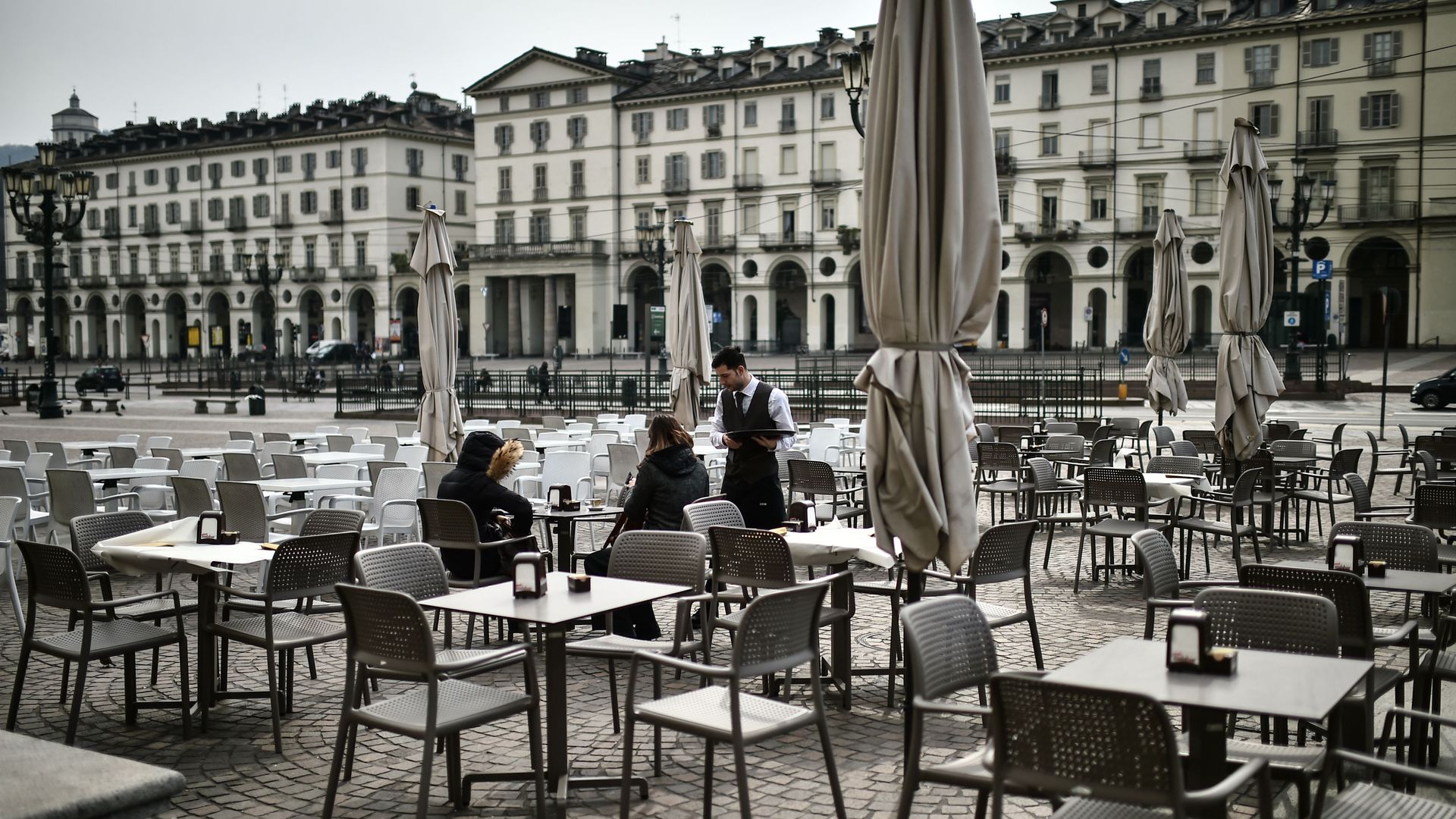 Customers order drinks at a deserted cafe terrace on Piazza Vittorio in Turin.