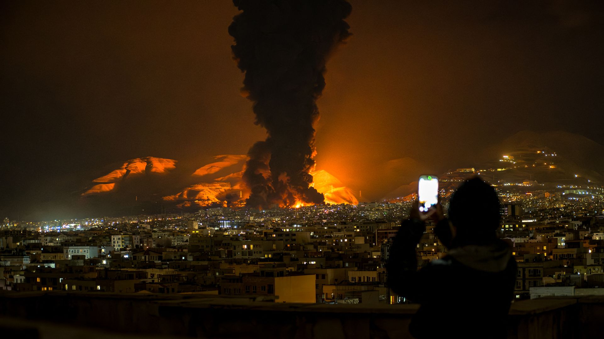 A woman takes video of an explosion in Tehran with her phone