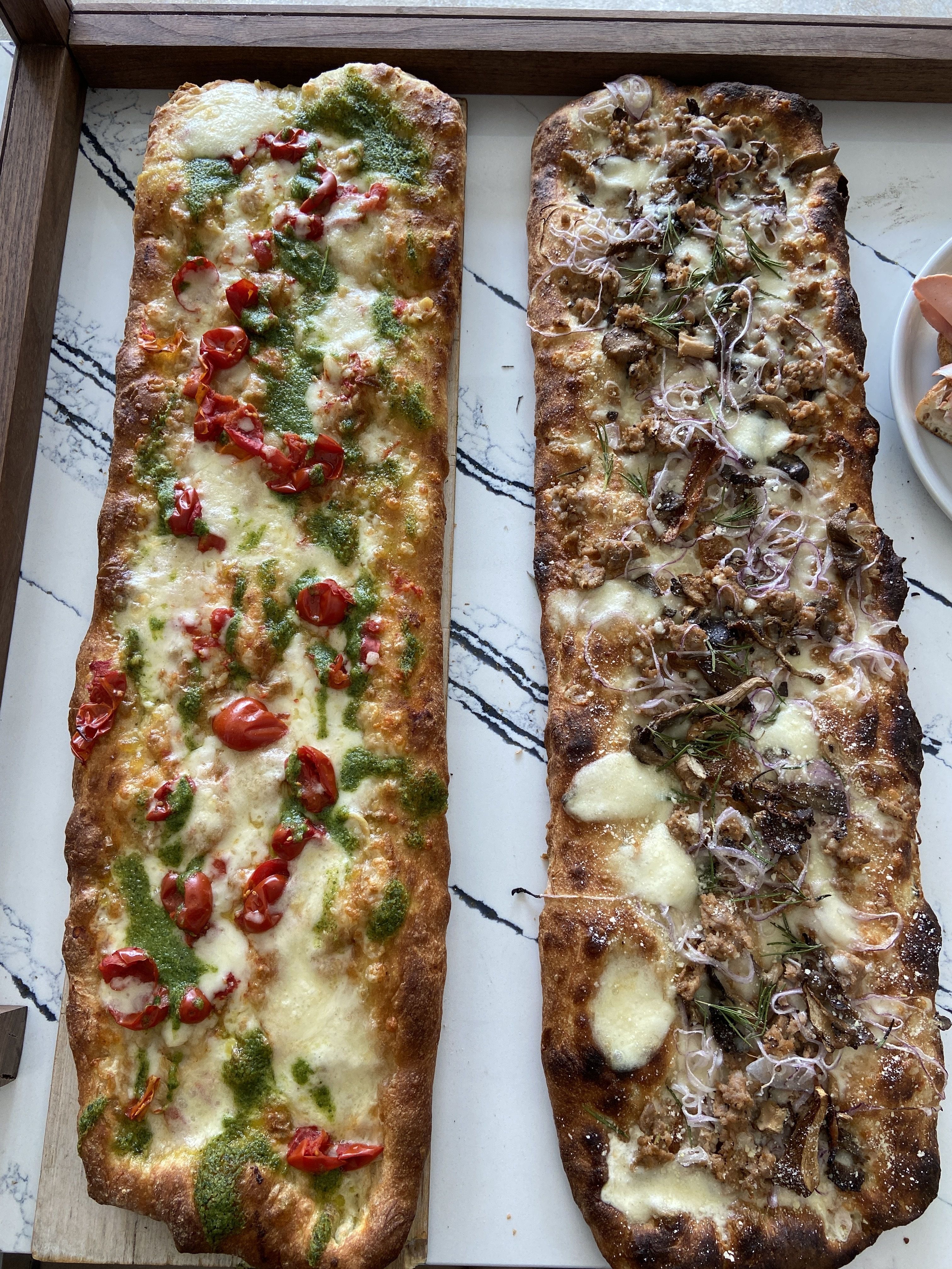 Pesto, burrata and tomato pizza (left) Sausage, mushroom and red onion pizza (front). Photo: Ashley Mahoney/Axios