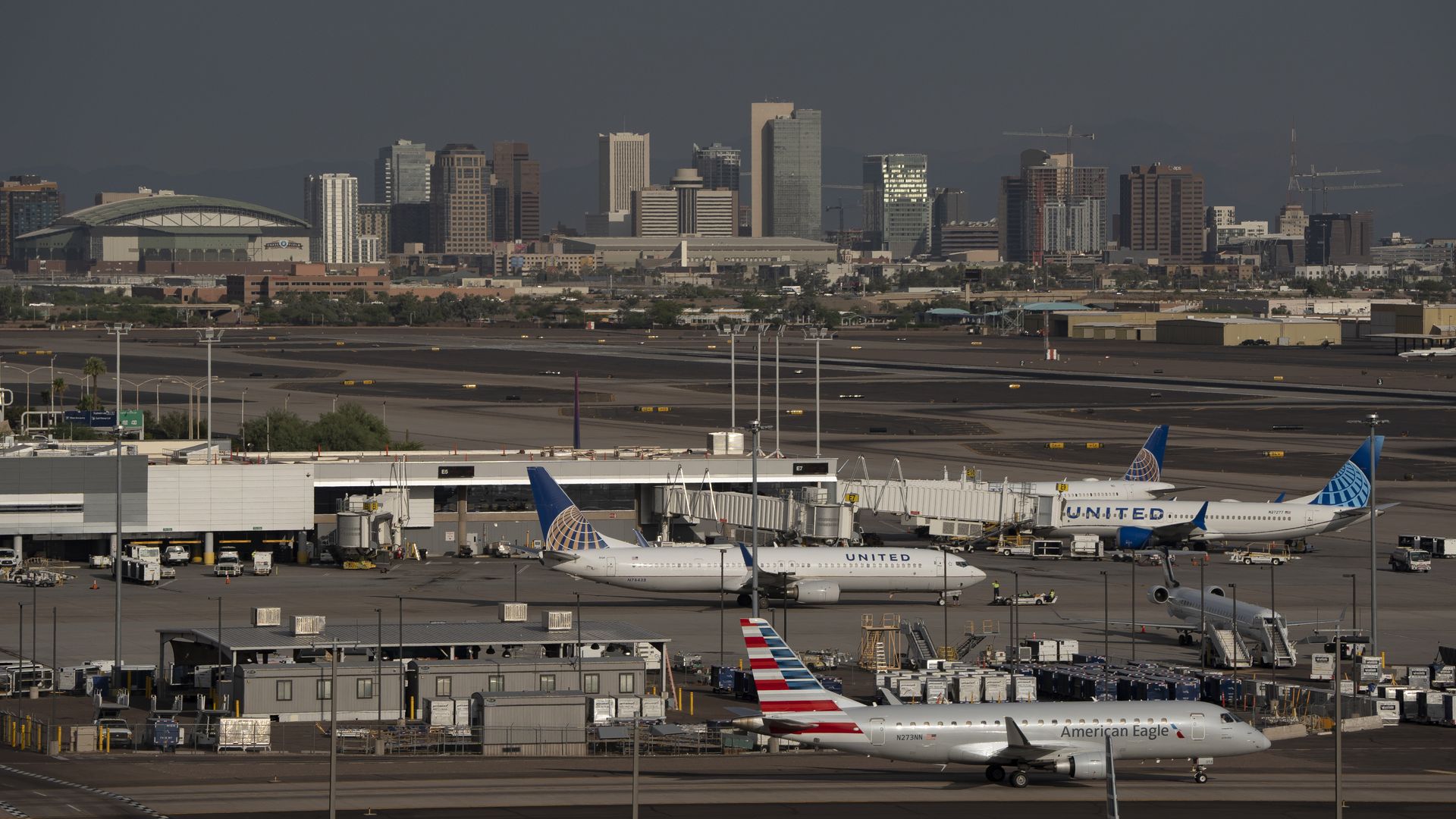 Several jetliners on an airport tarmac with the skyline of downtown Phoenix in the background.