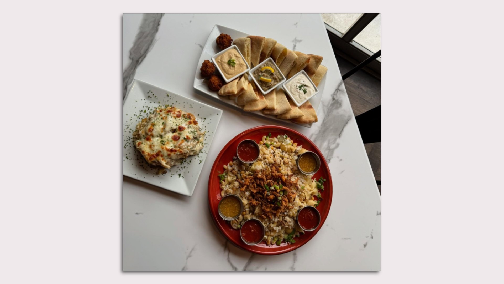 A spread of food with hummus, baba ganoush, feta cheese, falafel, pita bread, Koshari the most popular classic Egyptian dish, and Macarona Bechamel 