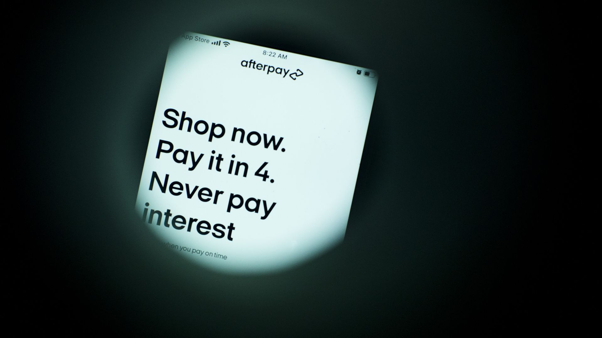 Close-up of a phone screen displaying Afterpay app with the text: "Shop now. Pay it in 4. Never pay interest." Black text on a white background with dark surroundings.