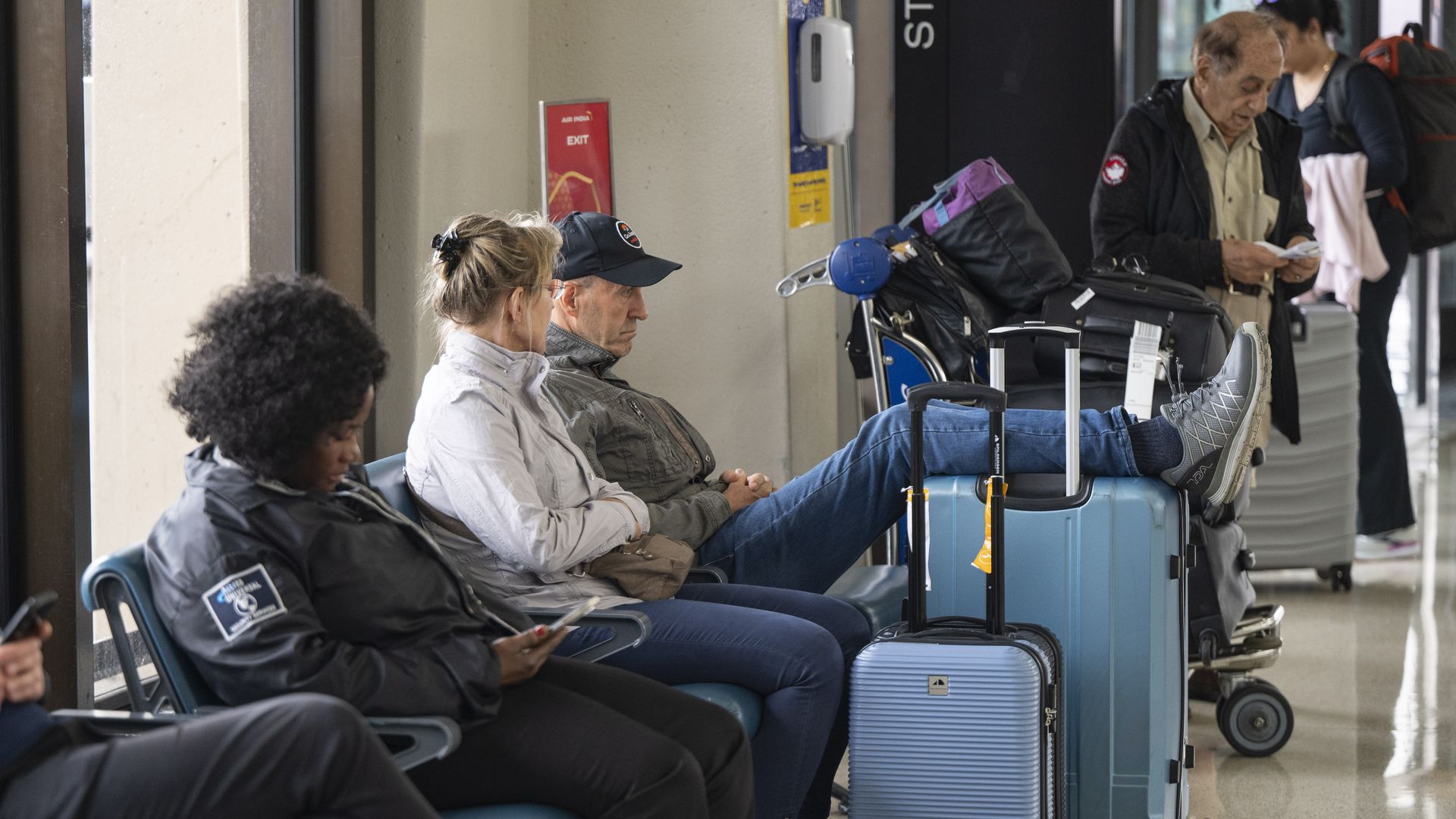 People sit at the airport, some with their legs resting on suitcases 