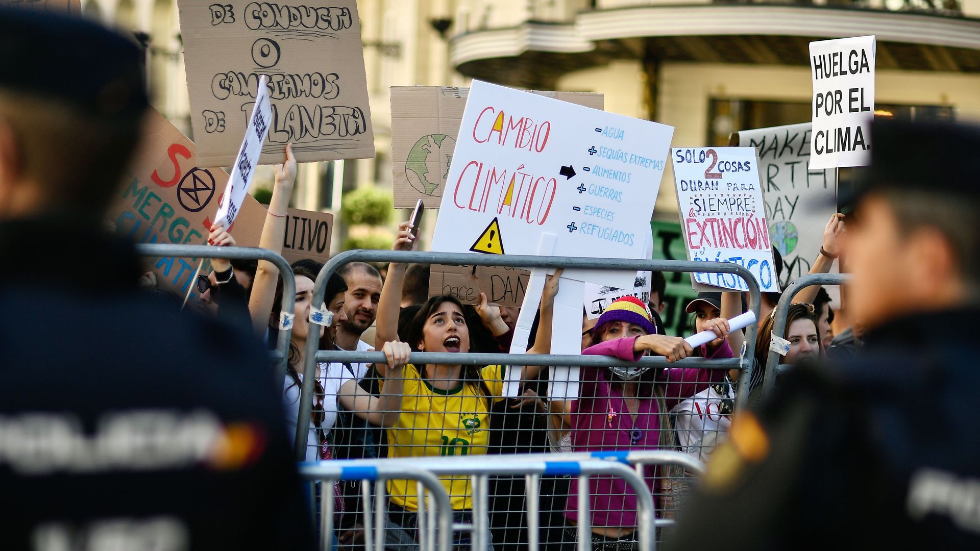 In this image, a child waves a sign from behind a metal gate at a protest in Spain.