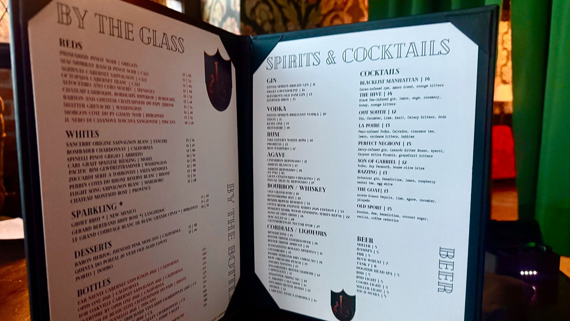 Open bar menu featuring wine by the glass, sparkling, desserts, bottles, spirits and cocktails, and beer lists in black text on white pages with a dark frame.