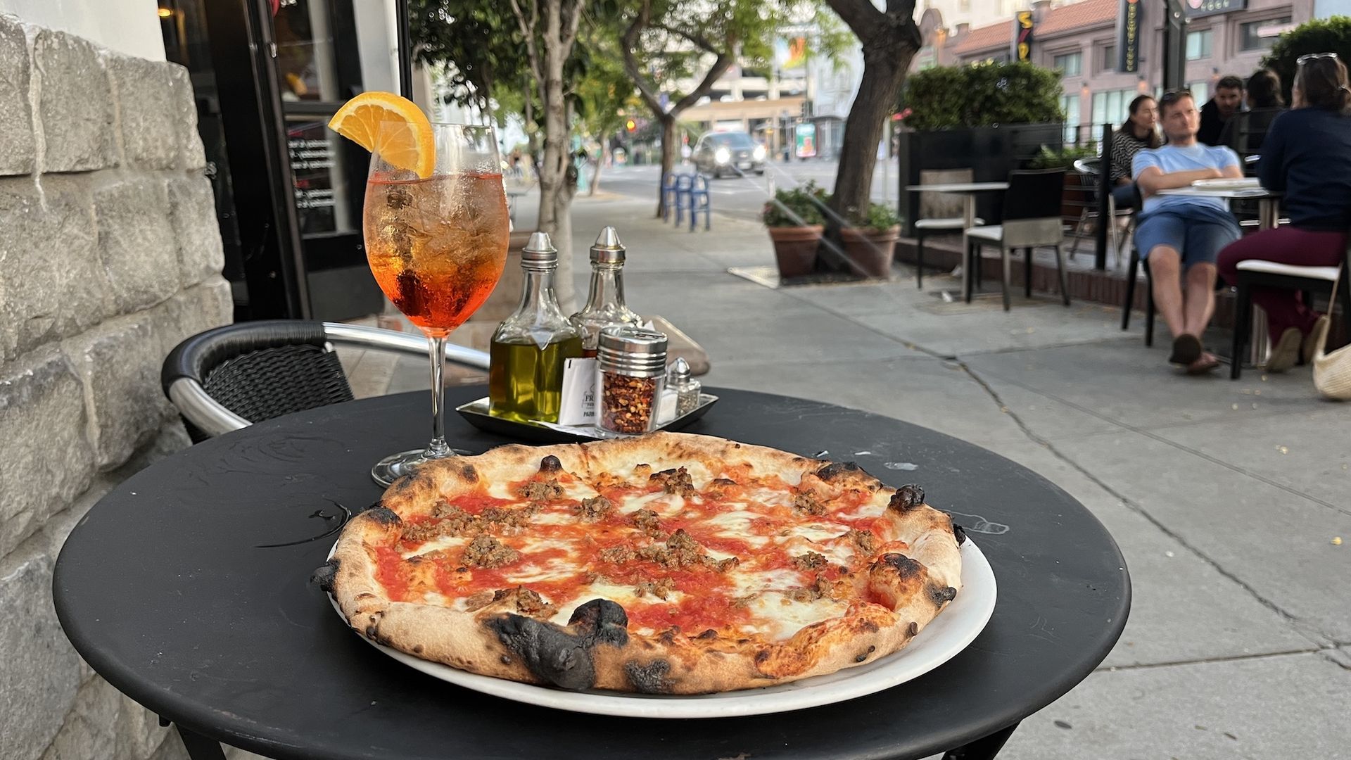 A pizza and an aperol spritz on a patio table.