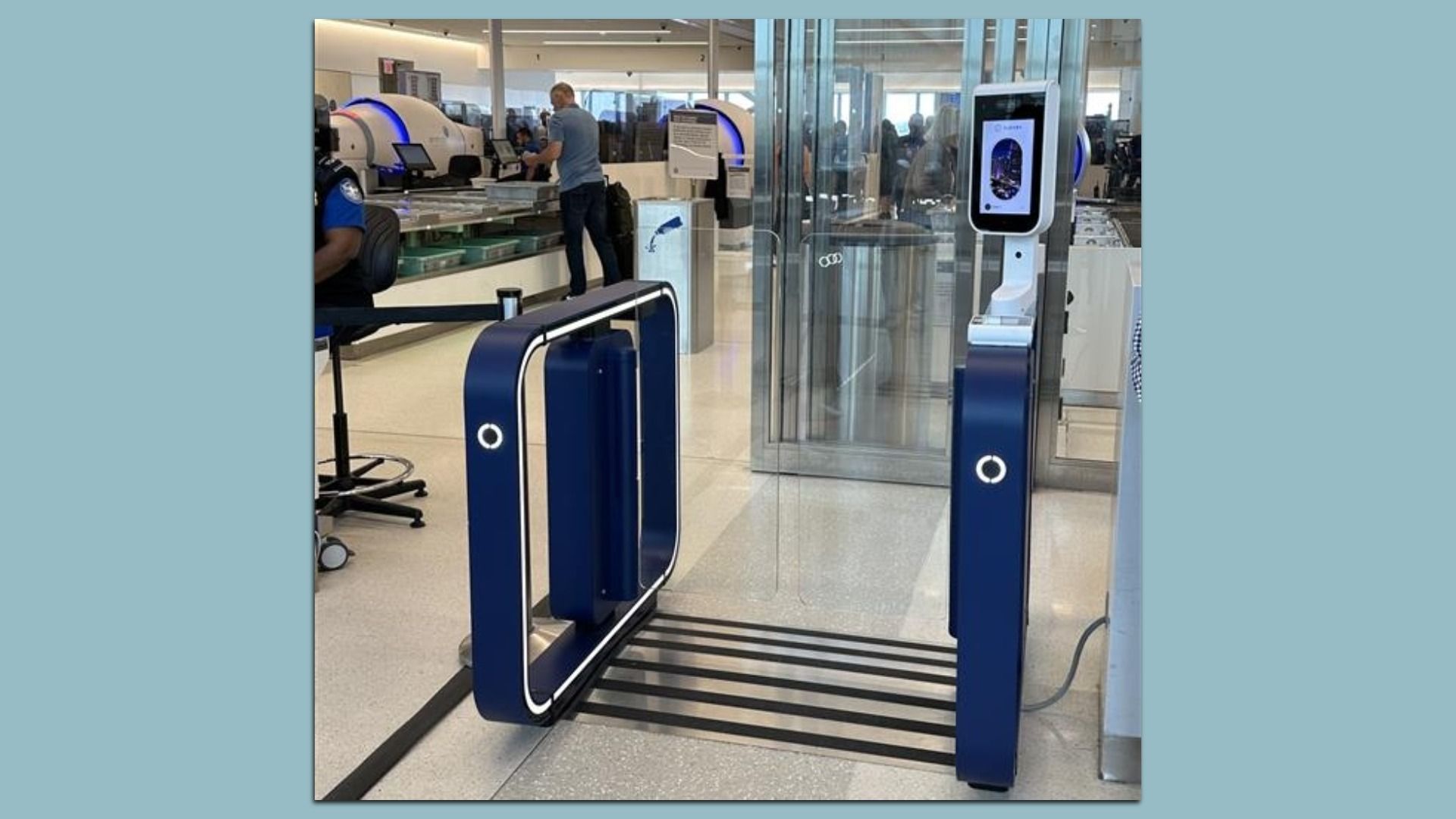 Airport security area with blue automated turnstiles, glass doors, and a touchscreen kiosk on the right. A staff member and passengers are seen at a counter in the background.